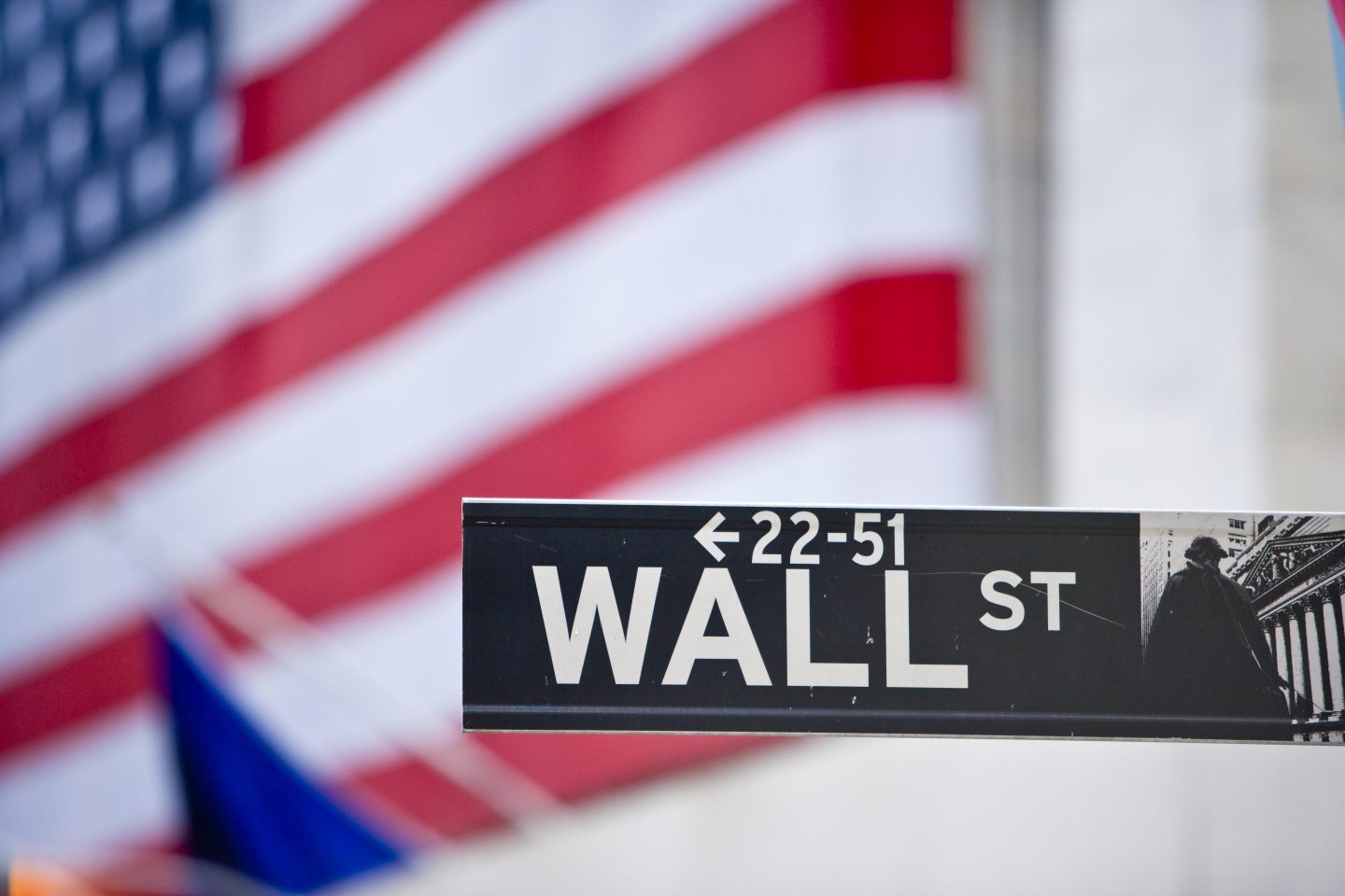 Wall Street sign, with a giant American flag in the background.