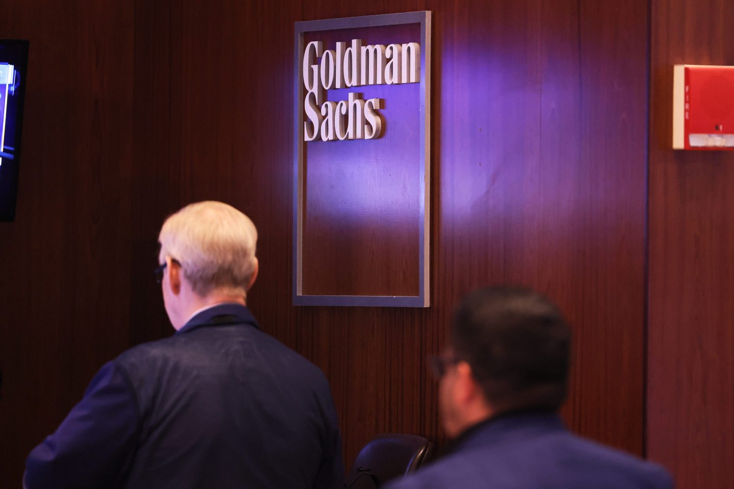 heads of People shown against a Goldman Sachs sign on a wall