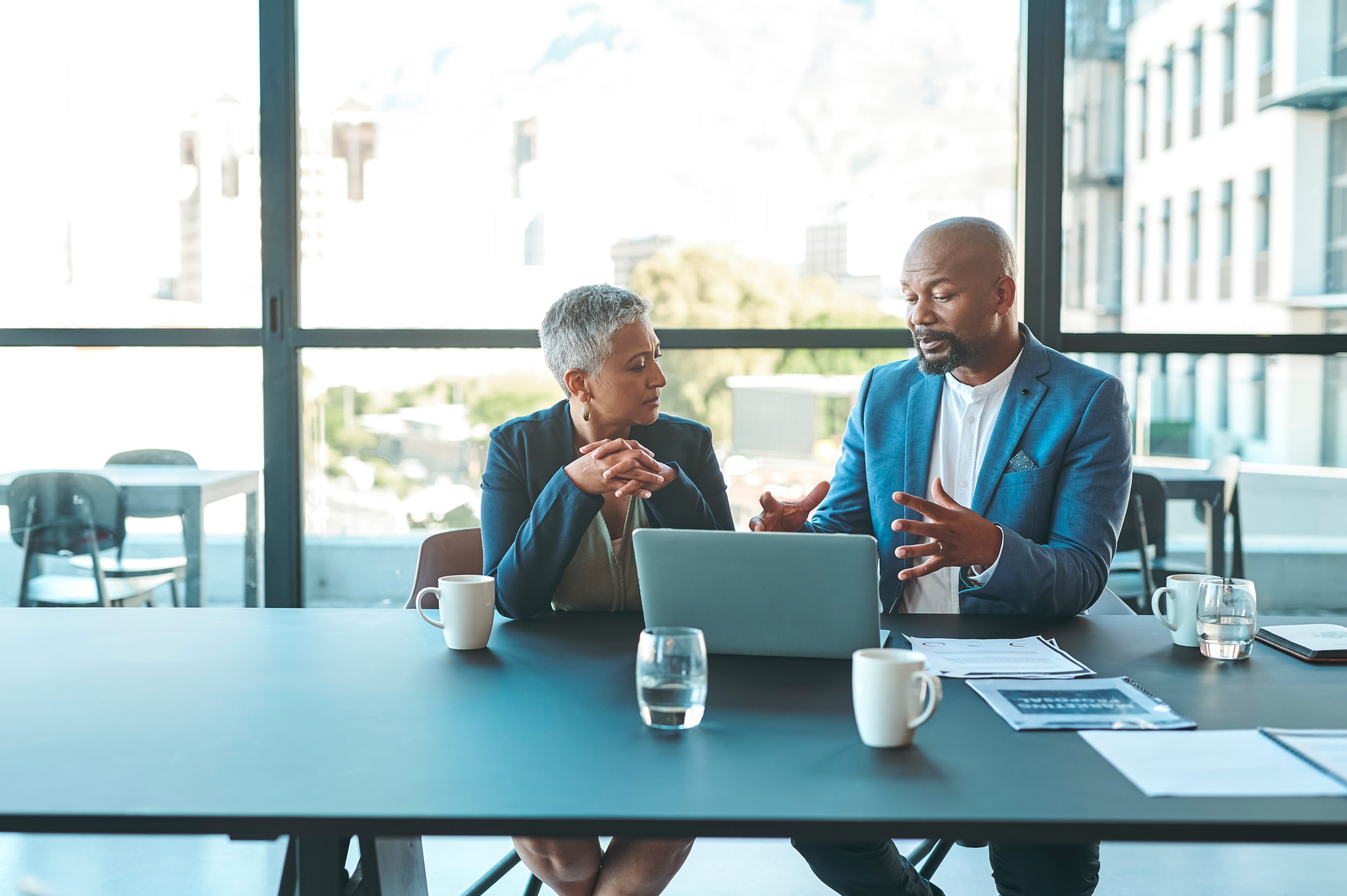 Two business coworkers sit and chat in a conference room.