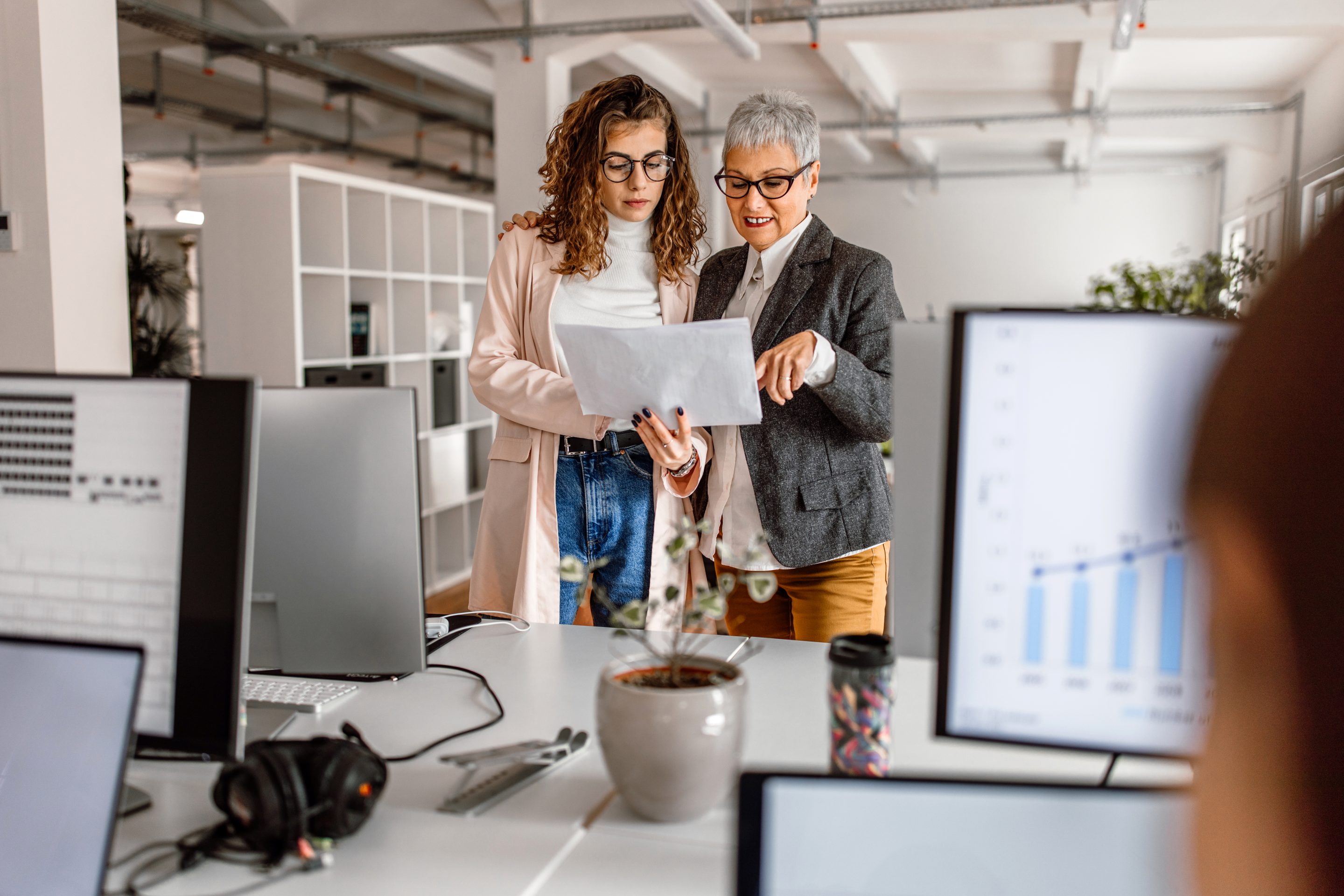 Two women, one older and one younger, converse together in an office.