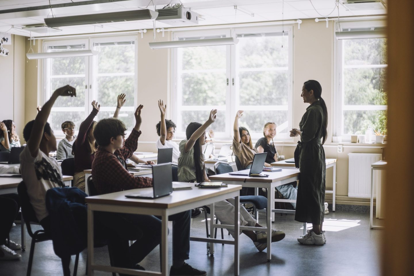 Students raising hands while teacher asking questions in class at school