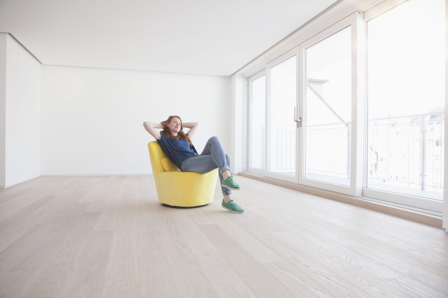 Woman lounging in yellow chair in empty apartment