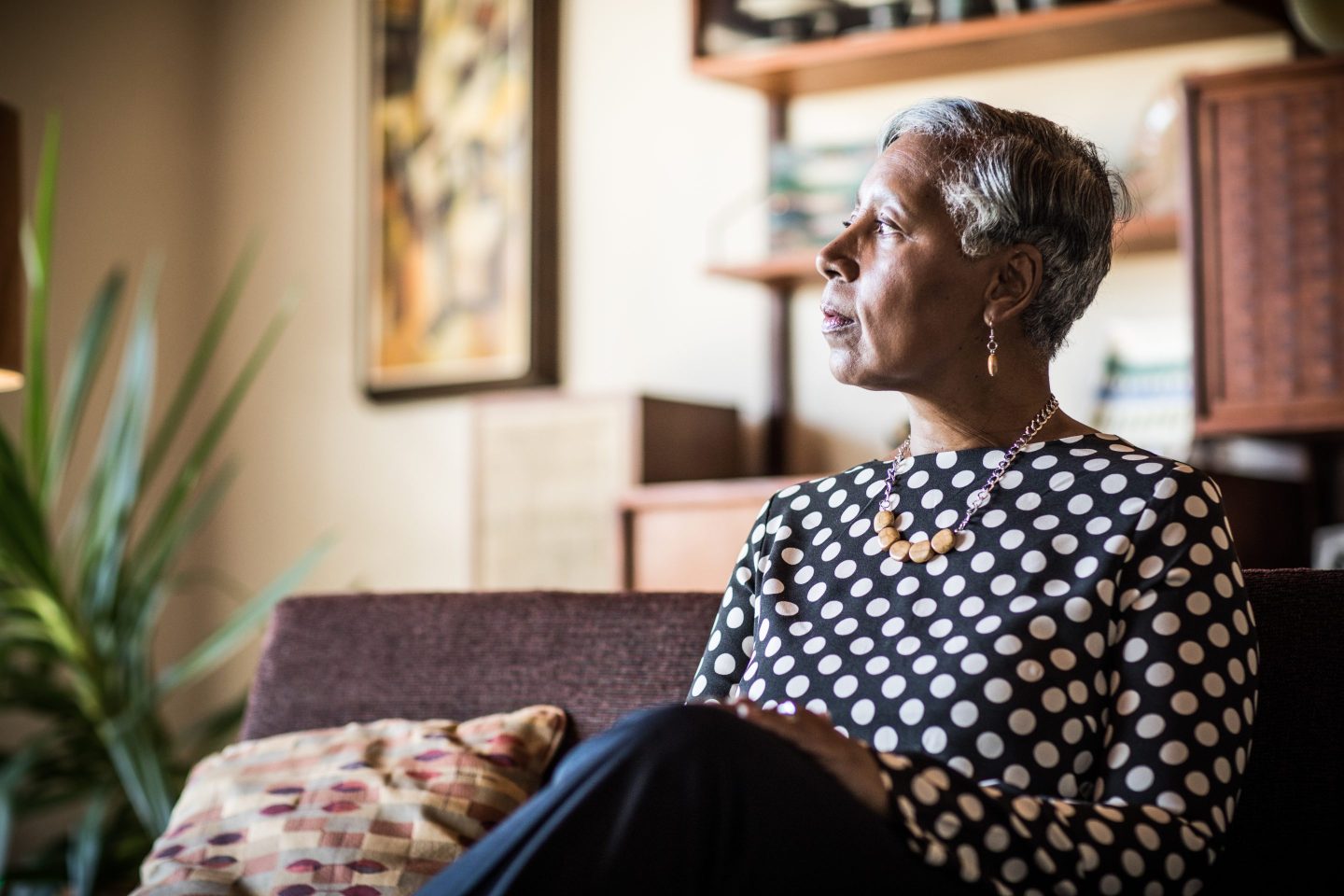 Photo of a woman looking pensive, sitting on a couch at home