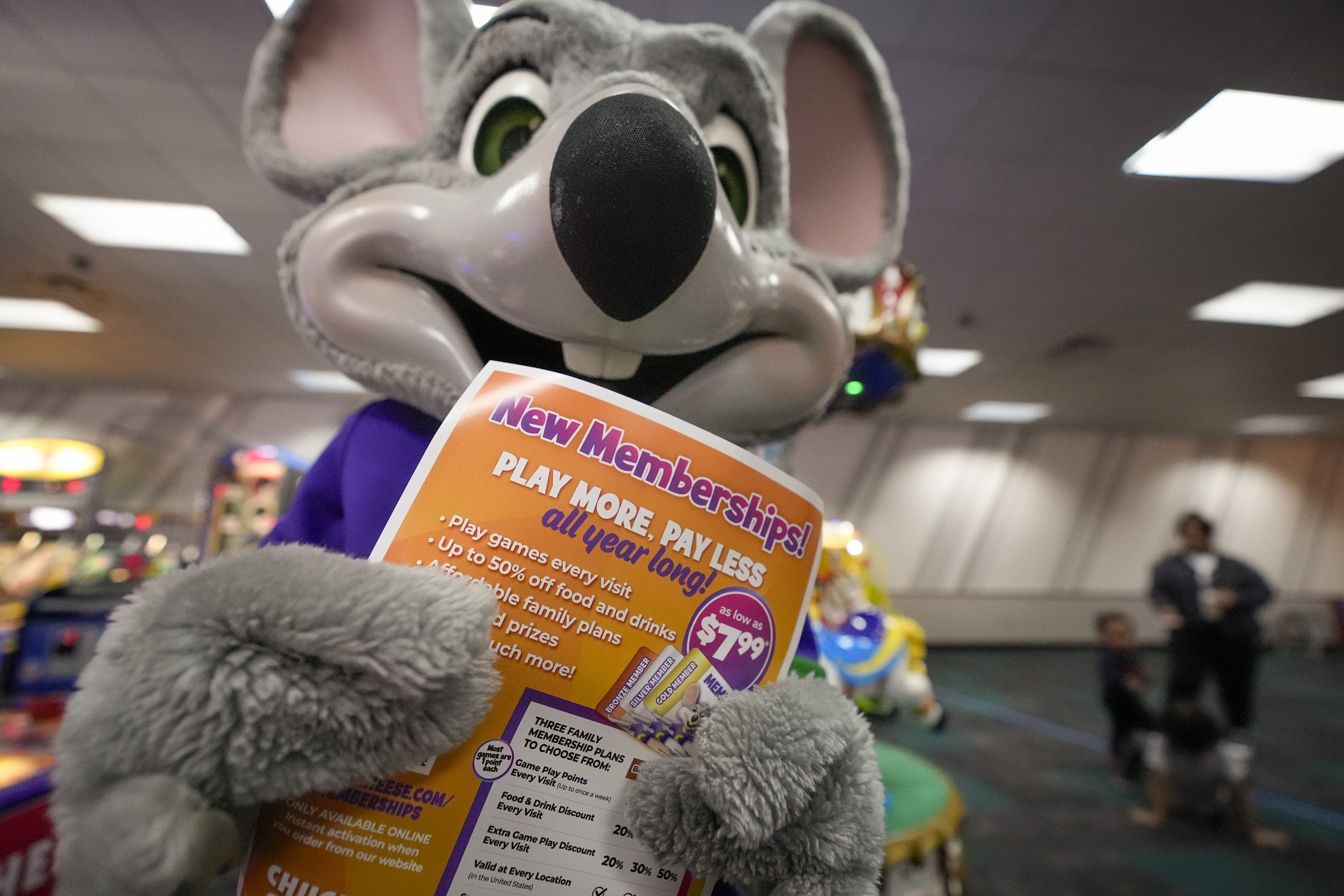 An employee dressed as Chuck E. Cheese holds a flyer advertising new memberships at a location on March 13, 2024, in San Diego.