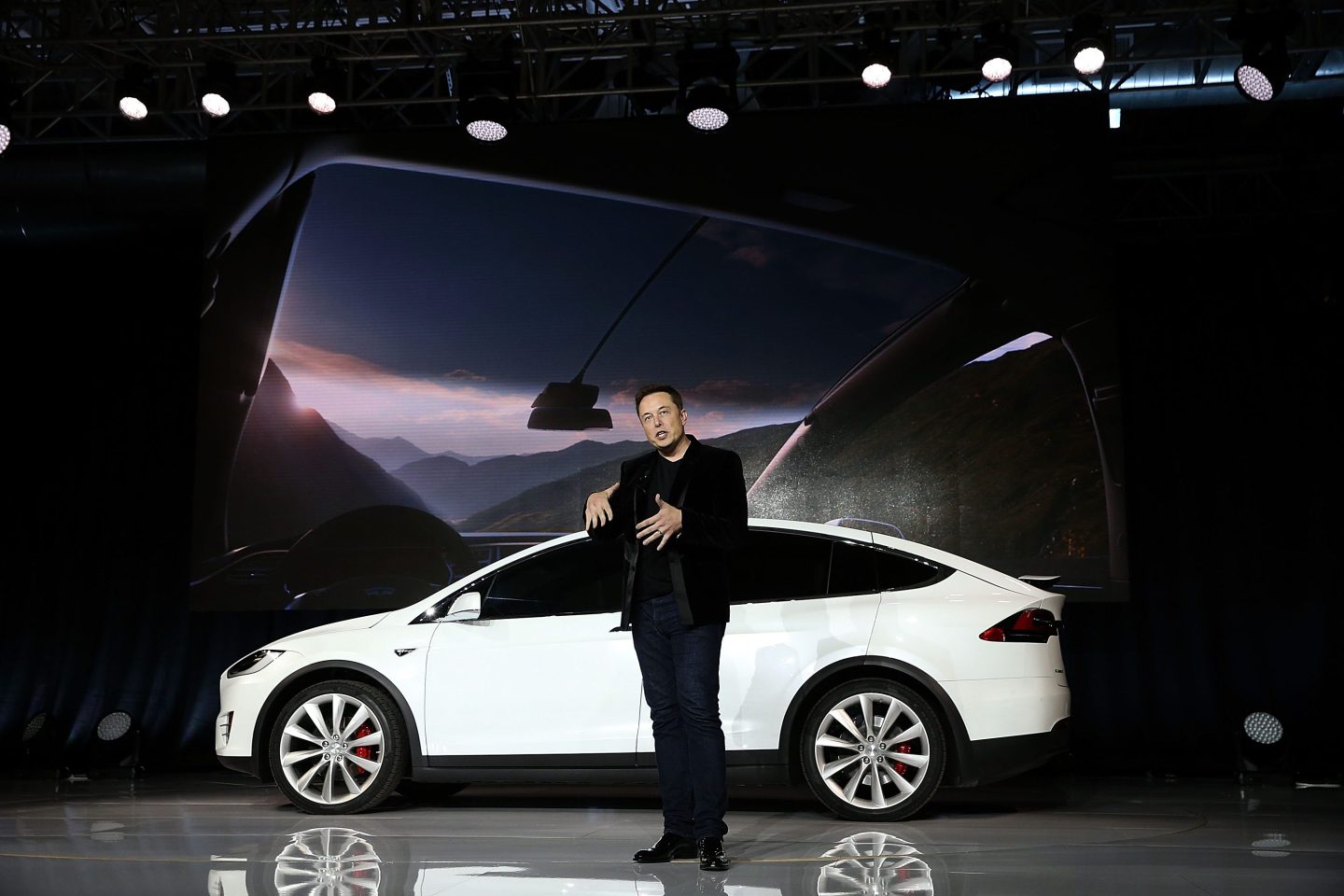 elon musk stands in front of a white car on a stage