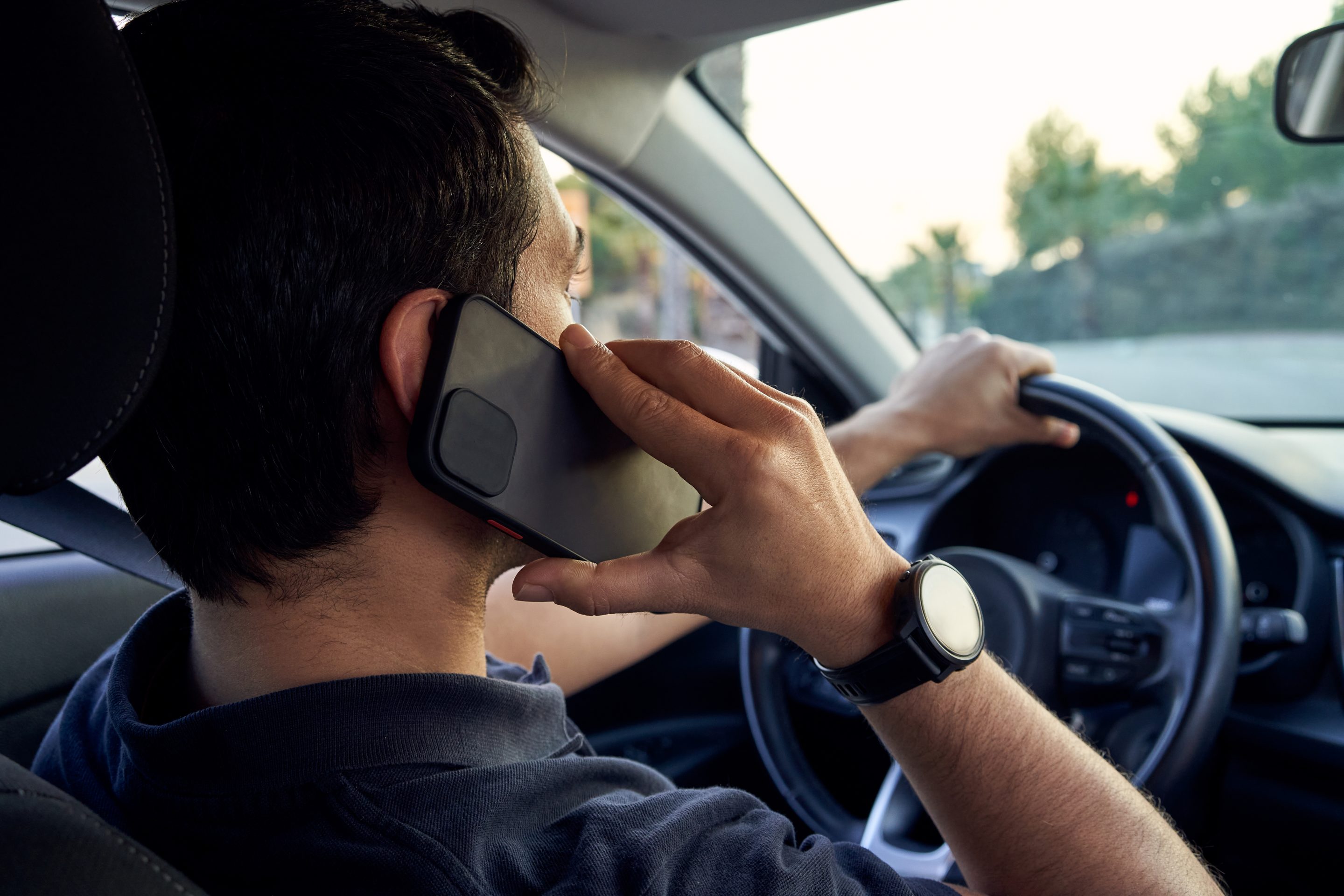 Rear view of a young unrecognizable Hispanic man talking on a smartphone while driving his car
