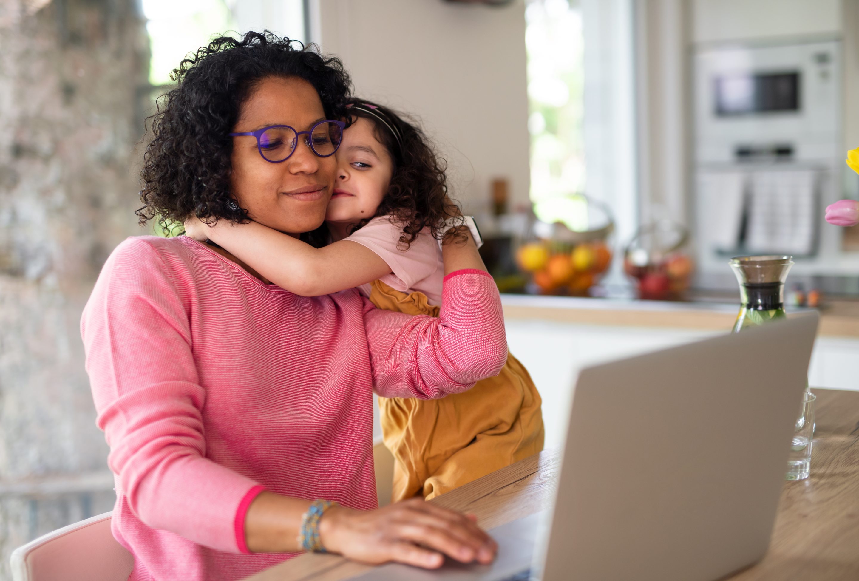 A girl hugging her mother who is working from home. 