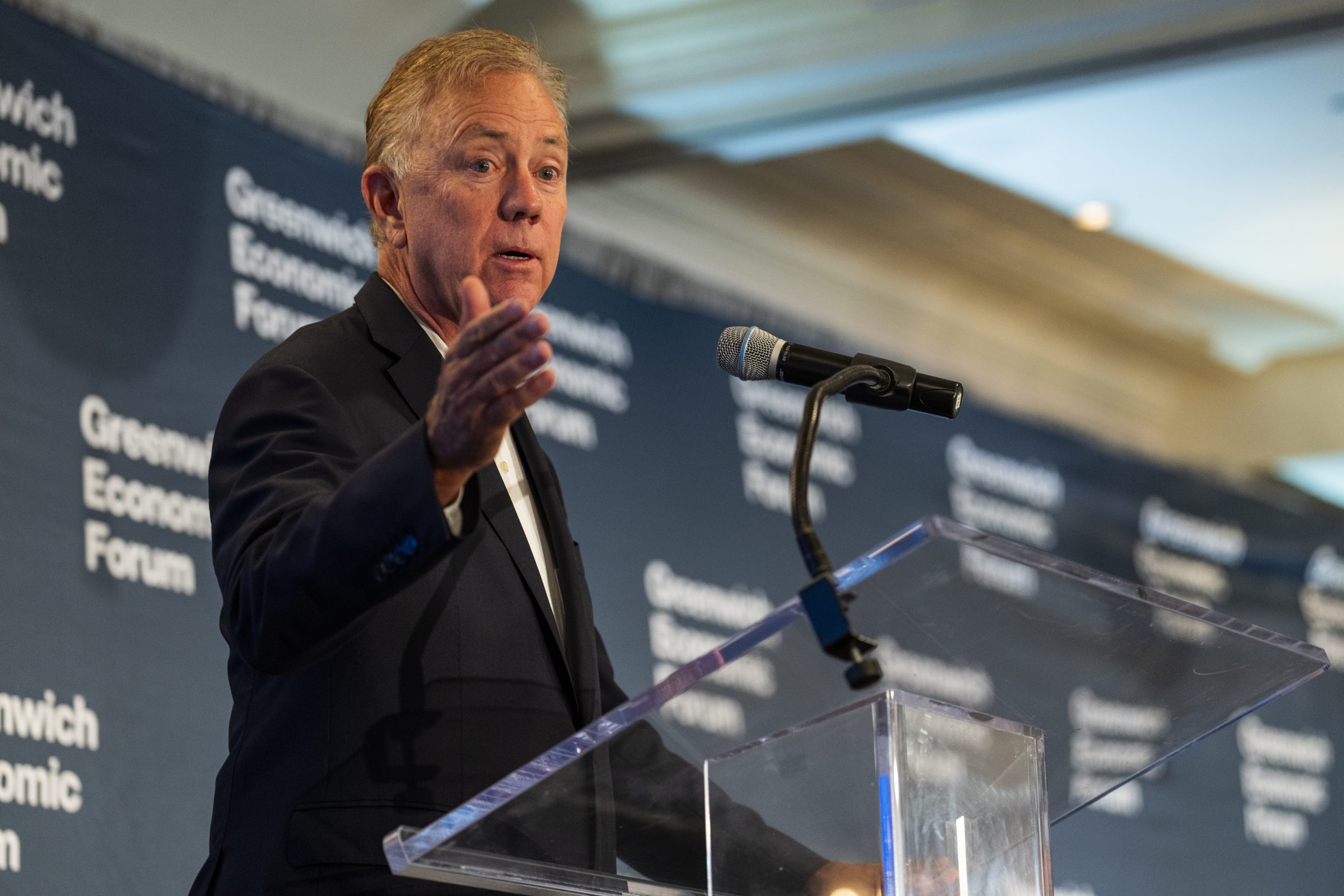 Connecticut Governor Ned Lamont standing at a podium giving a speech and raising his right arm.