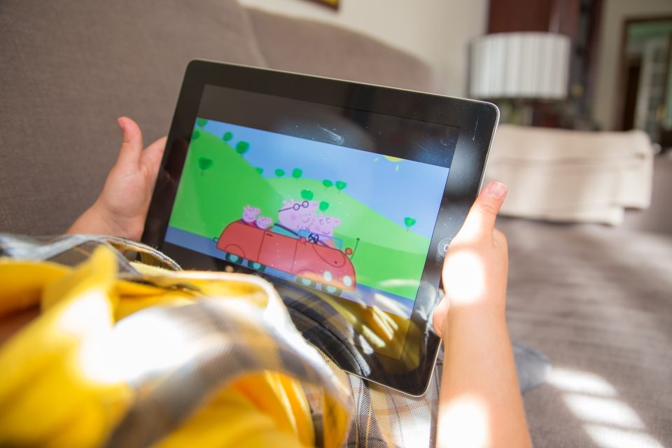 Girl watching cartoons online with the iPad tablet laying in the sofa at home.