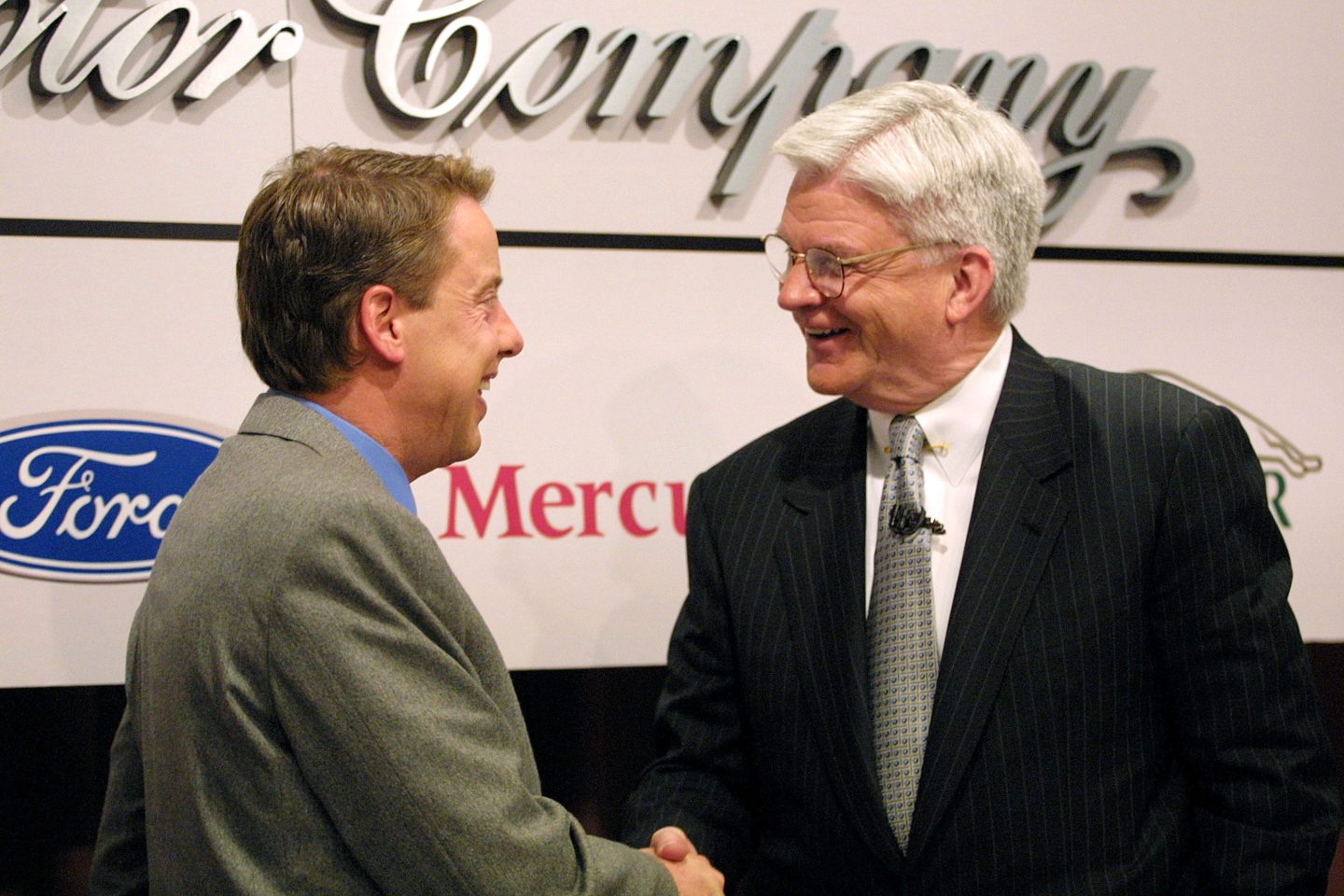 Two men shake hands with the Ford logo behind them