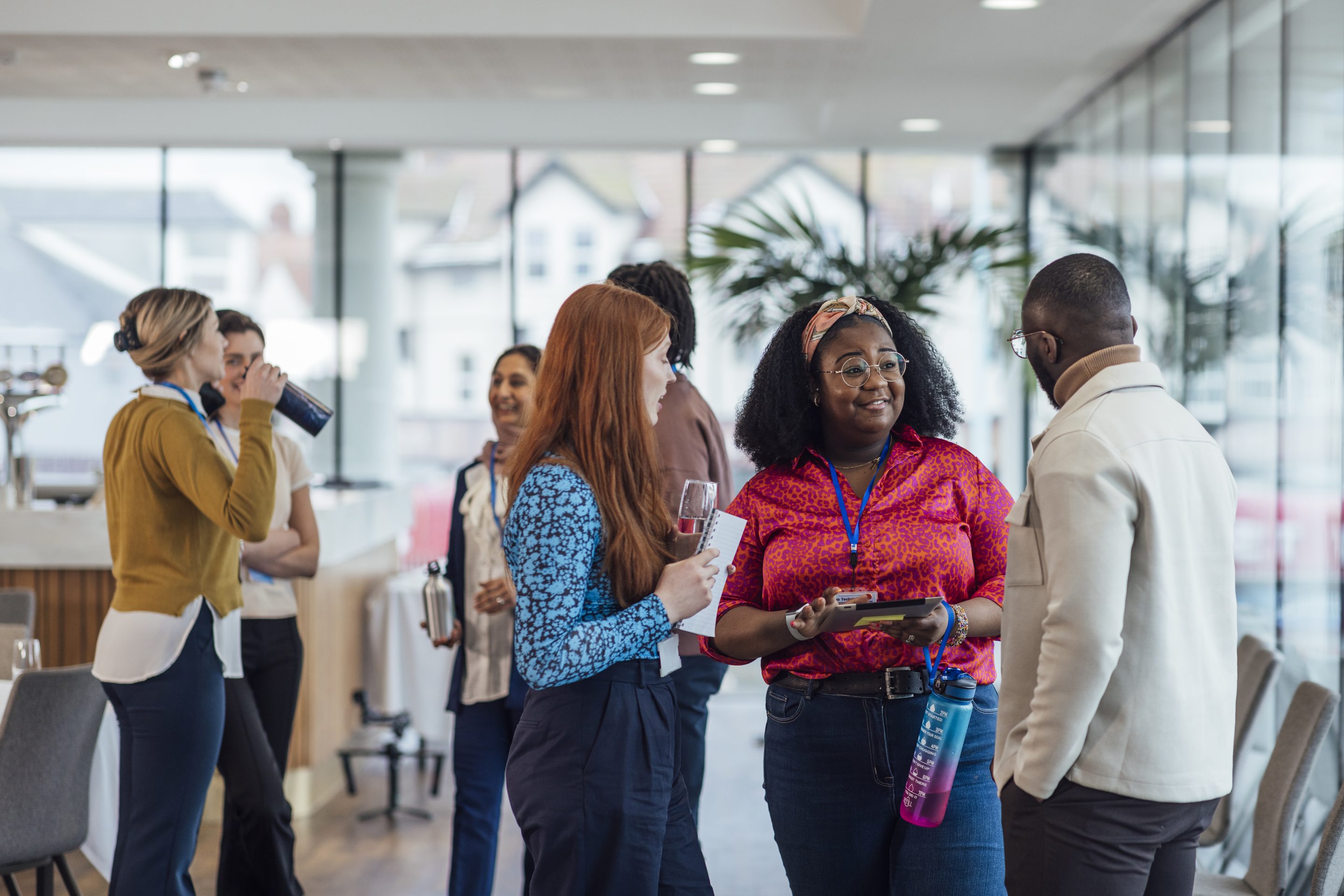 A group of people dressed in business casual attire stand and converse in a meeting room.