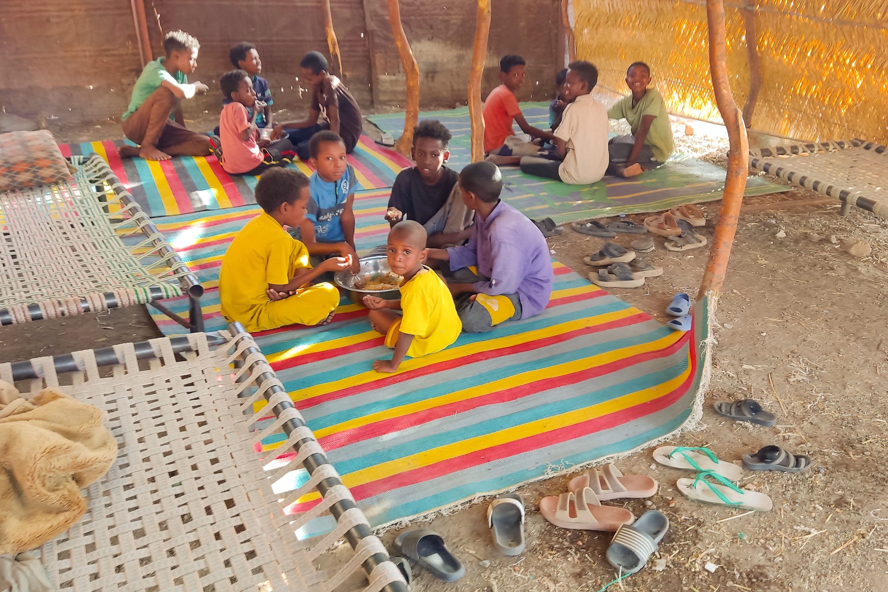 Children sit together sharing a large bowl of food, as Sudanese families host internally displaced people coming from the central Sudanese state of Gezira to the eastern Sudanese city of Gedaref on June 3, 2024.