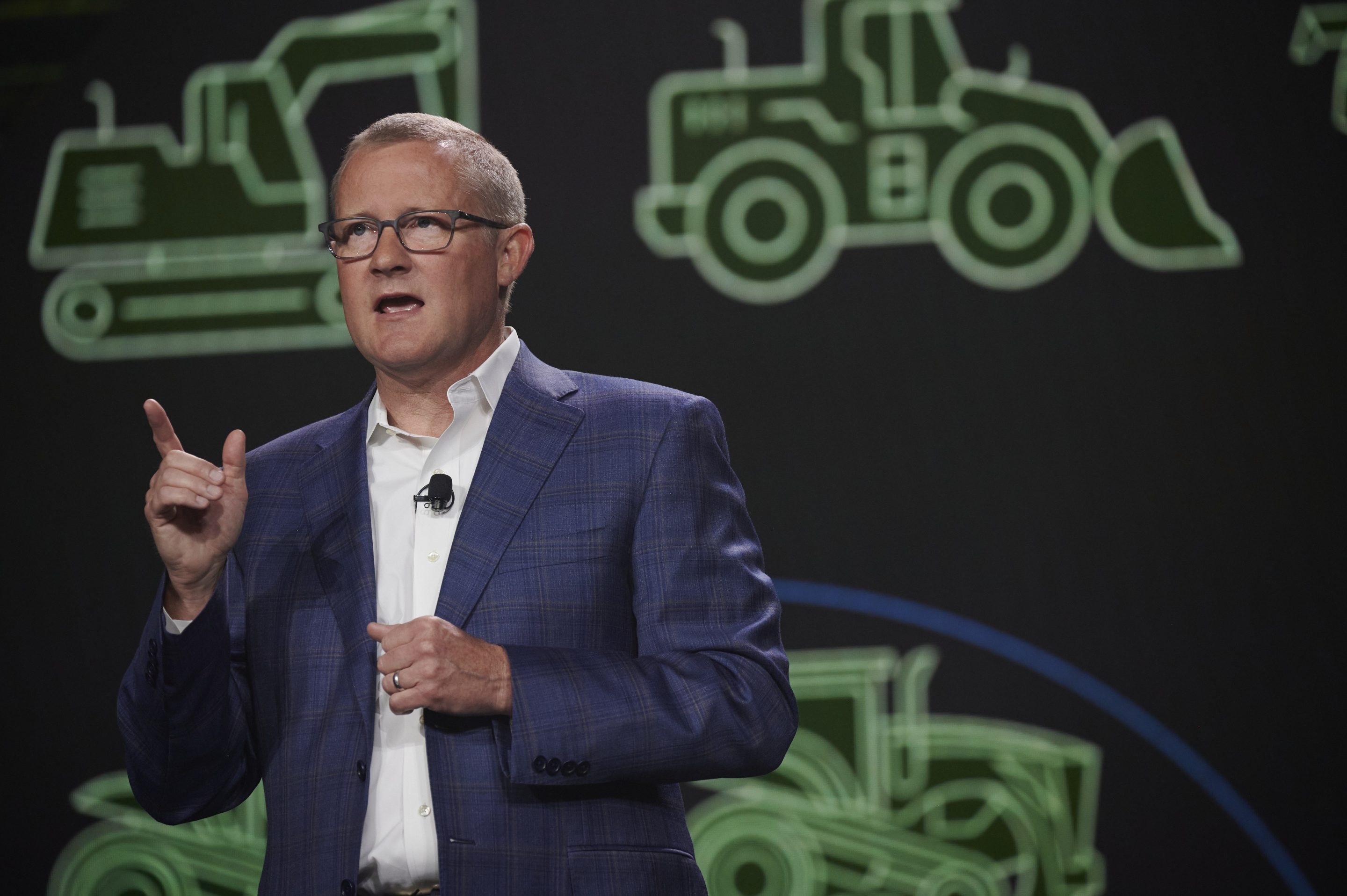 John May stands in front of a gray background with green tractors.
