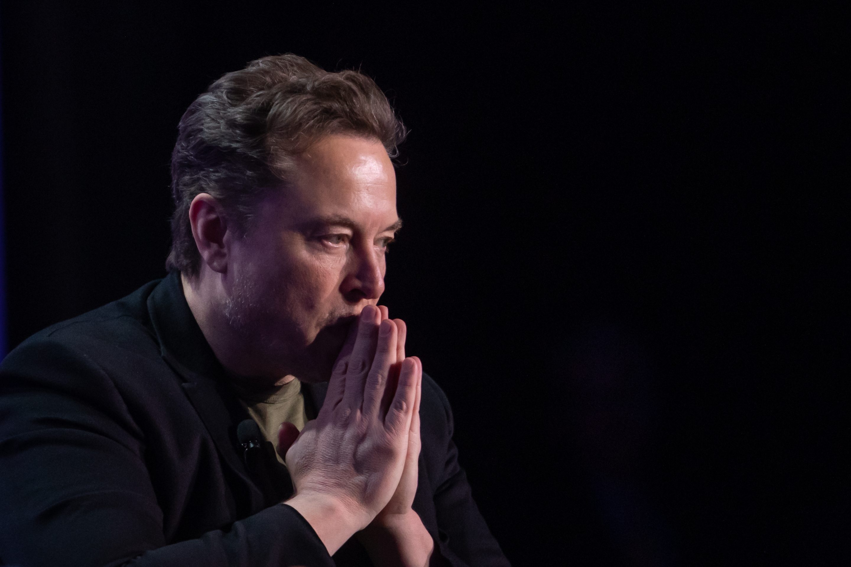 Musk holding his hands in front of his face, looking pensive