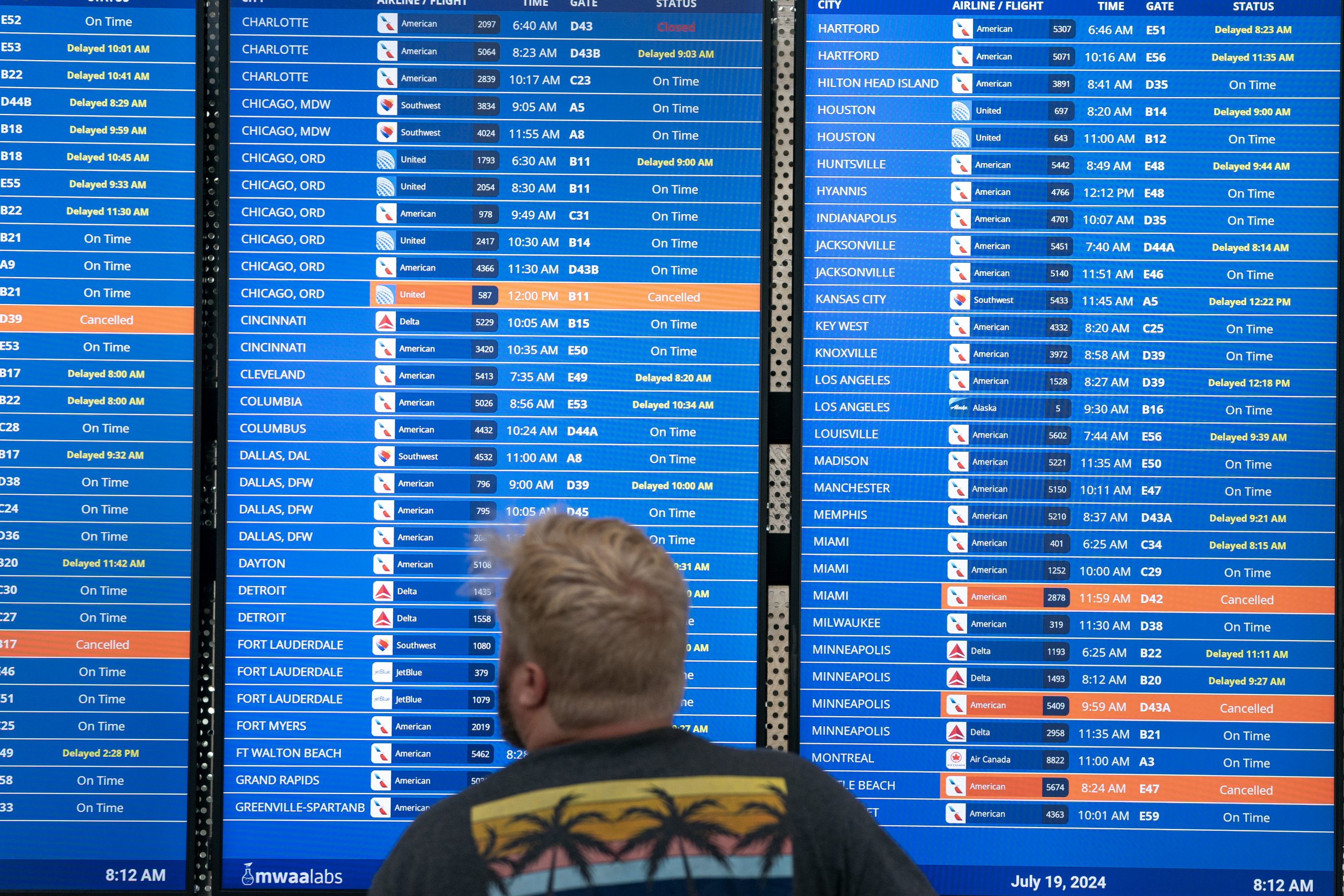 A man looks at an airport's board of delayed flights after the CrowdStrike outage
