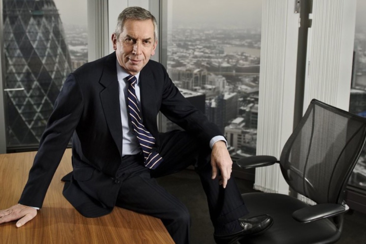 Terry Smith of Fundsmith sits on a table in a skyscraper verlooking the Gherkin in London.