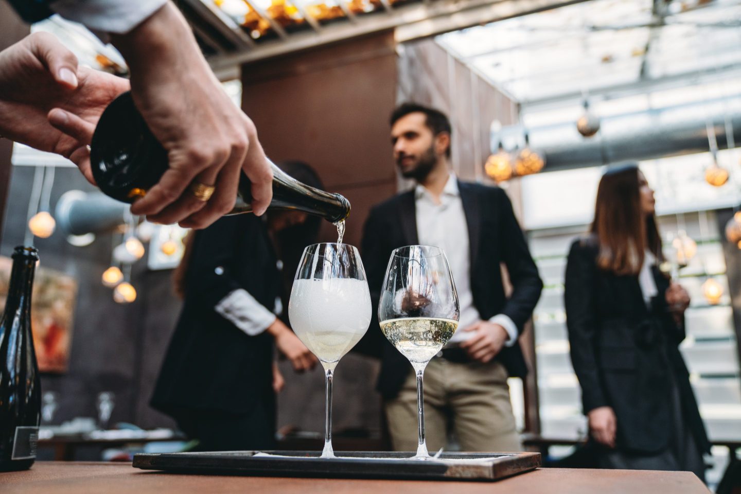 A waiter is pouring prosecco into glasses at the restaurant. High end luxury restaurant. Business people in the background.