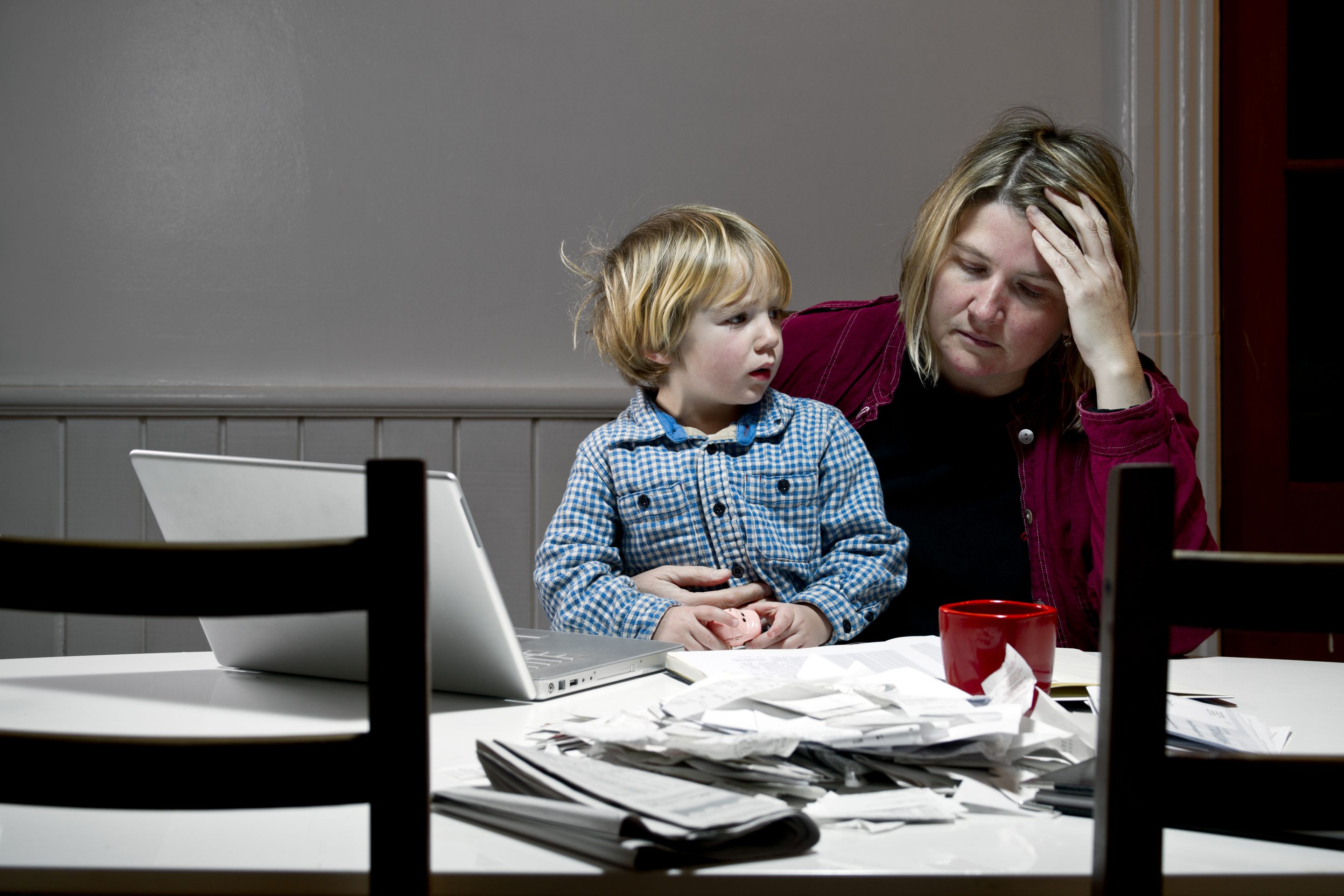 Mother struggles to pay bills with child in lap.