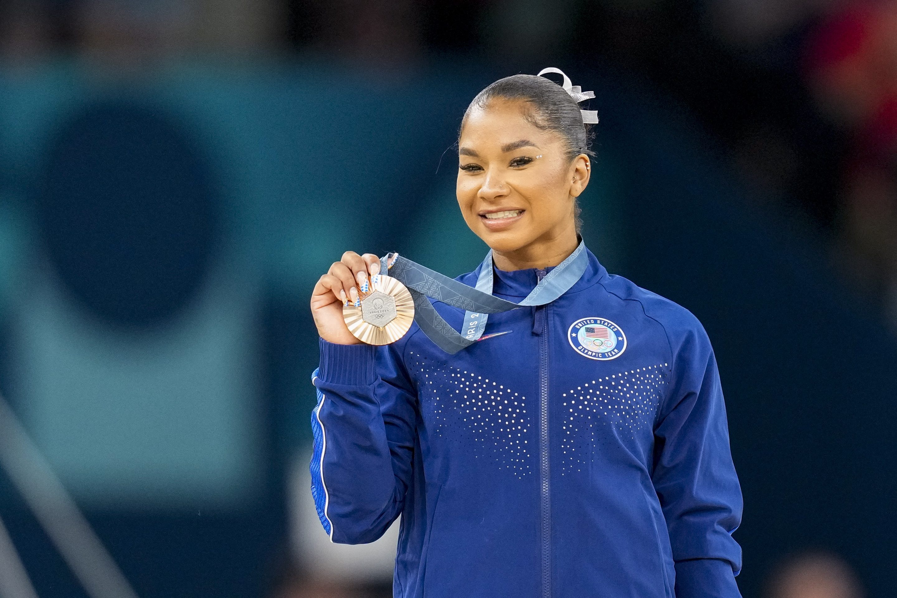 A woman smiles as she holds up her bronze medal