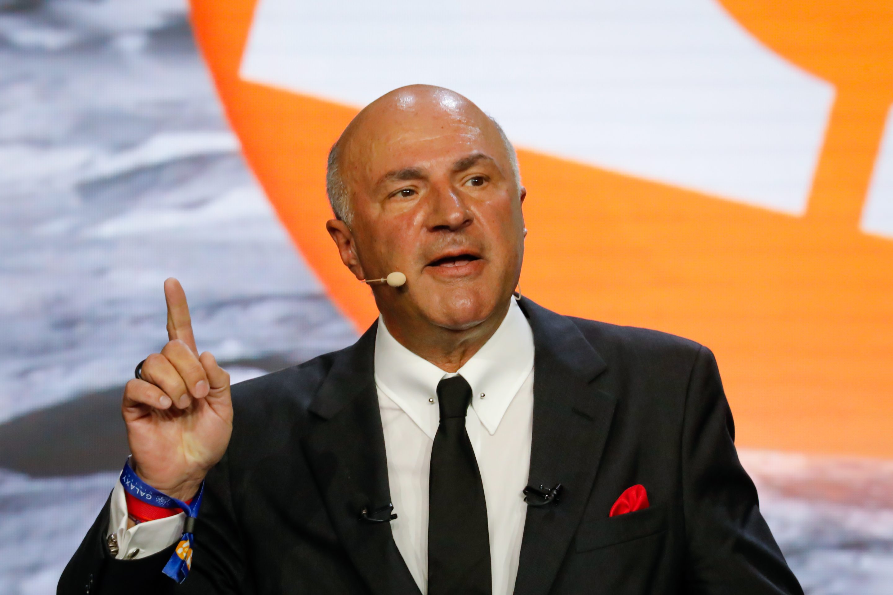 Kevin O'Leary speaks into a headset with his index finger raised in the air.