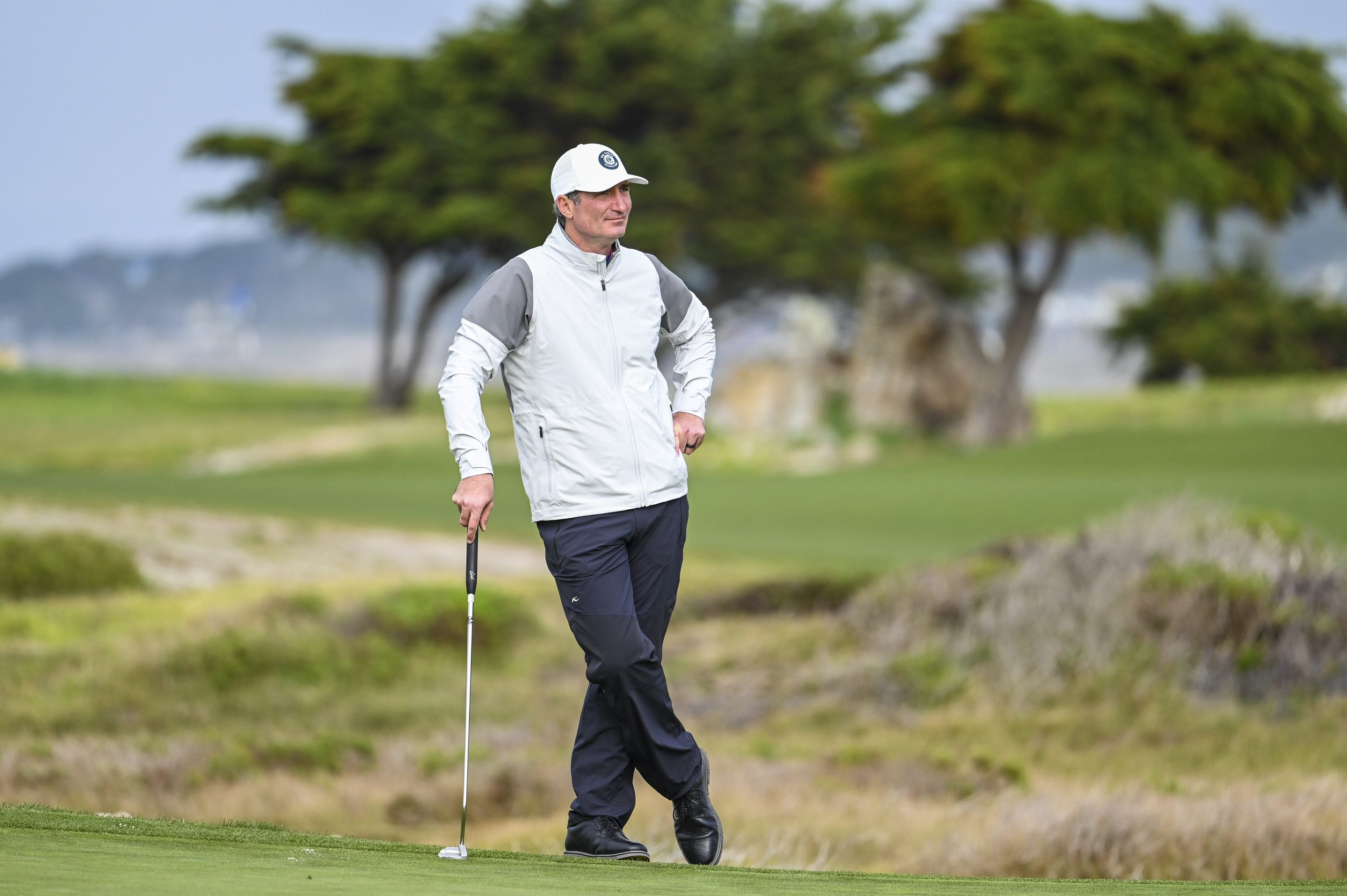 Brian Niccol leans on a golf club in the middle of a golf course.