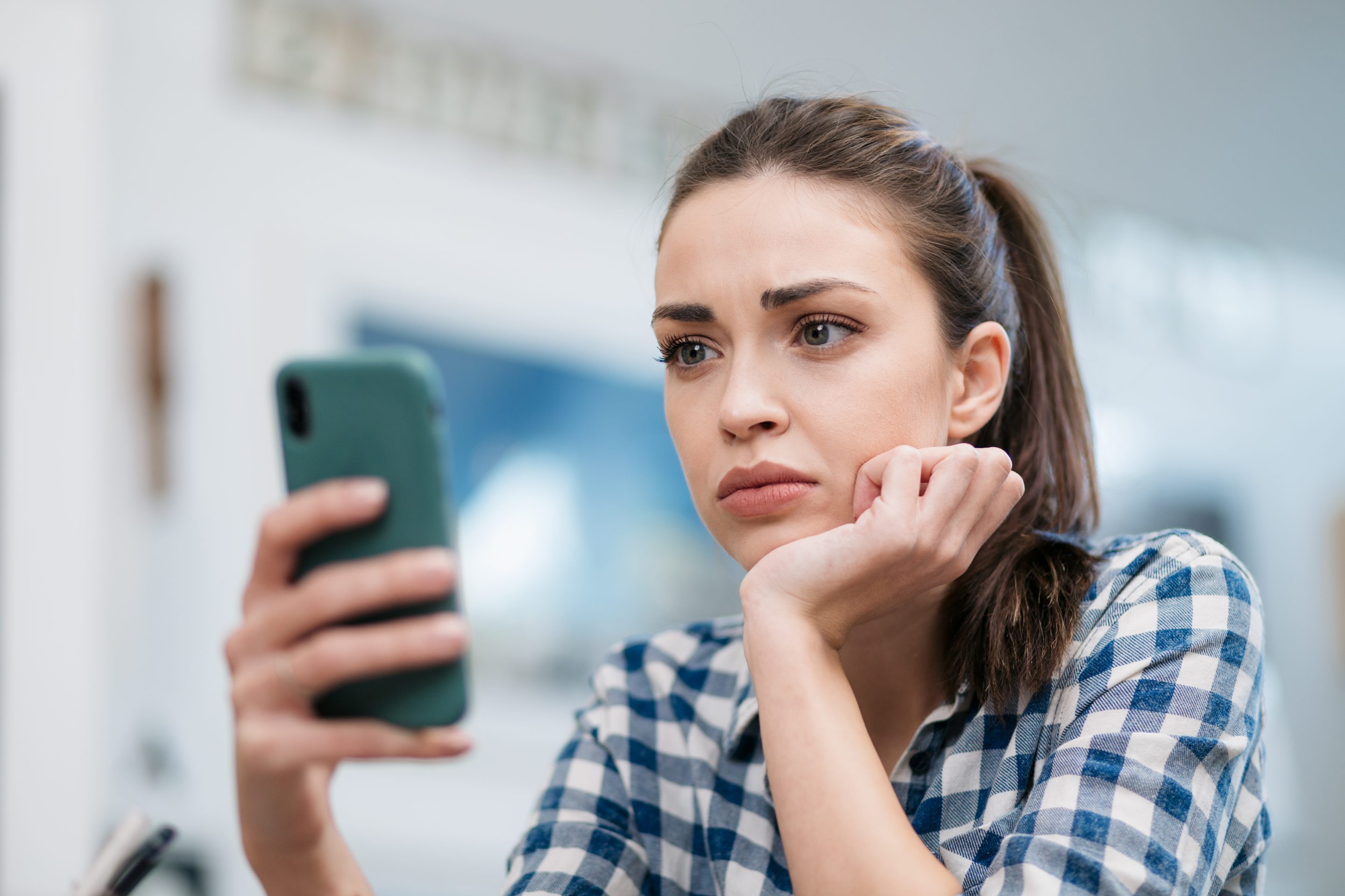 A women rests her chin in her hand and looks at her phone sadly.
