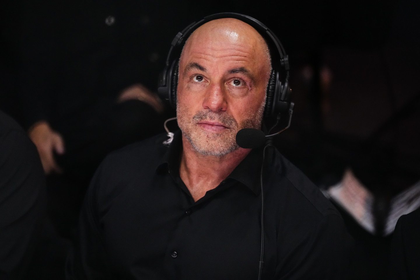 oe Rogan looks on during the UFC 306, he is wearing black and a black headset with microphone.