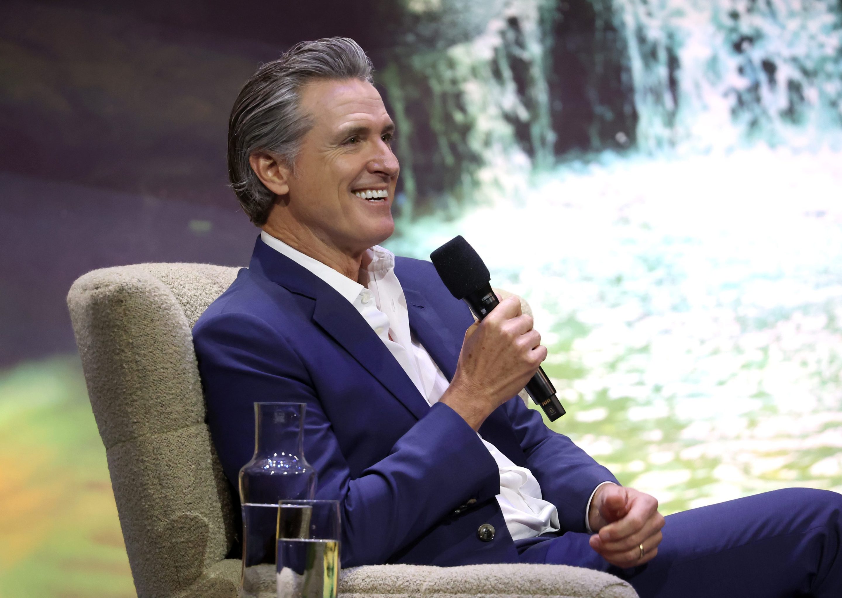 Governor newsom smiles holding a microphone on stage