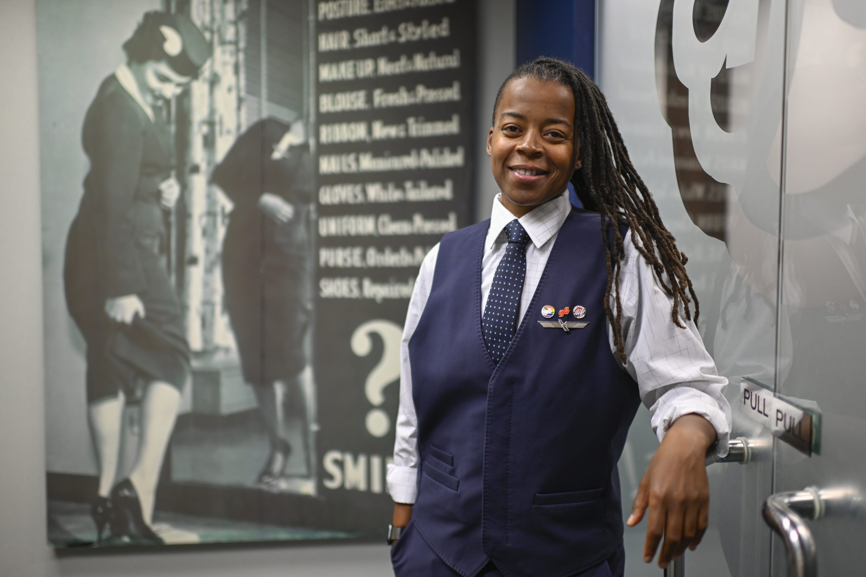 Keturah Johnson, international vice president for flight attendant union AFA-CWA, poses by a decades old, outdated poster with rules and uniforms for flight attendants, at her headquarters office, ob Sept. 18, 2024, in Washington.
