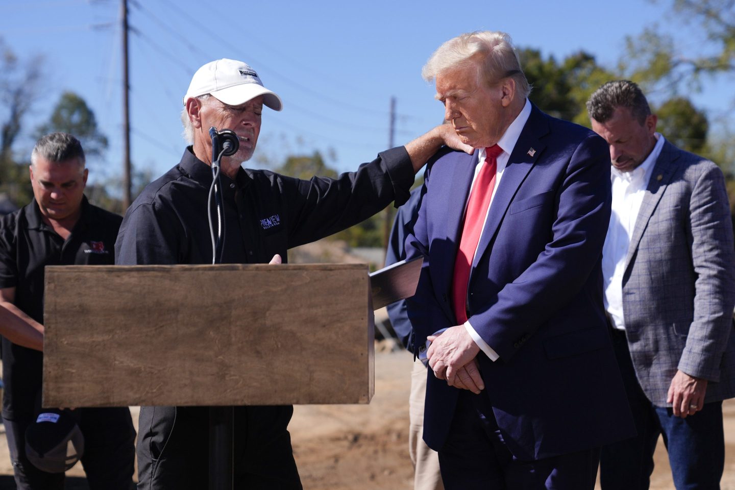 Republican presidential nominee former President Donald Trump prays with Mike Stewart, owner of Pine View Buildings, and others, after delivering remarks on the damage and federal response to Hurricane Helene.