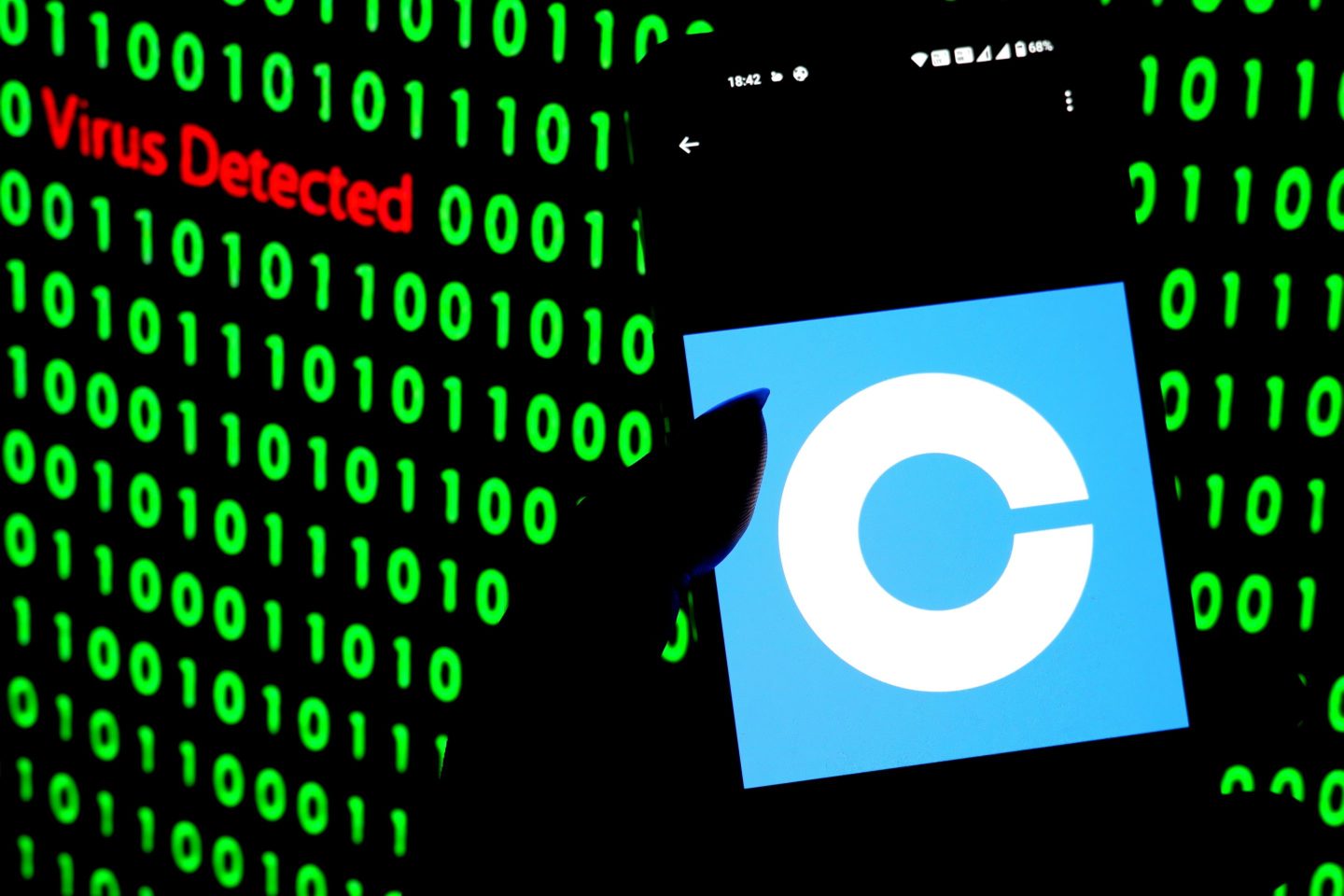 A Coinbase logo on a phone in front of a background of zeros and ones that says "Virus Detected"