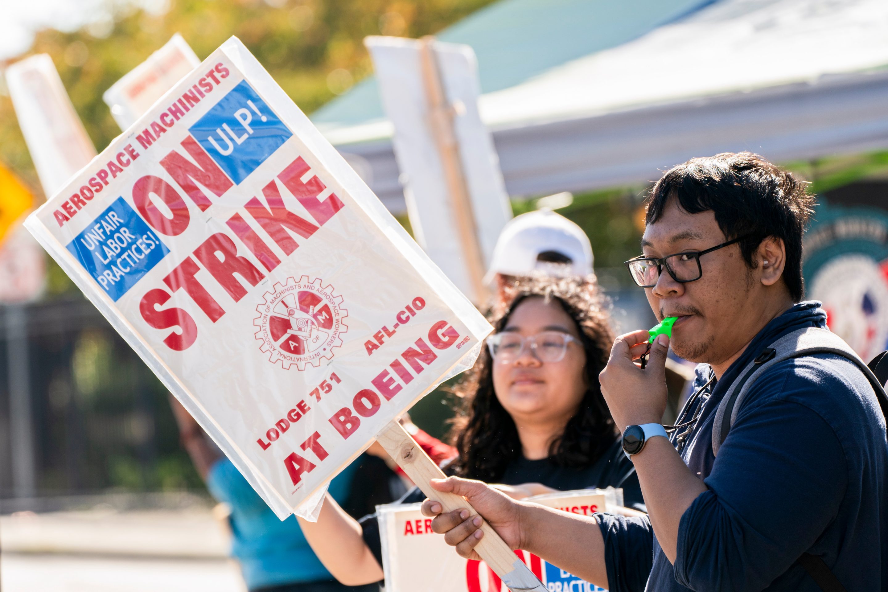 A man blows into a whistle and holds up an "ON STRIKE" sign.