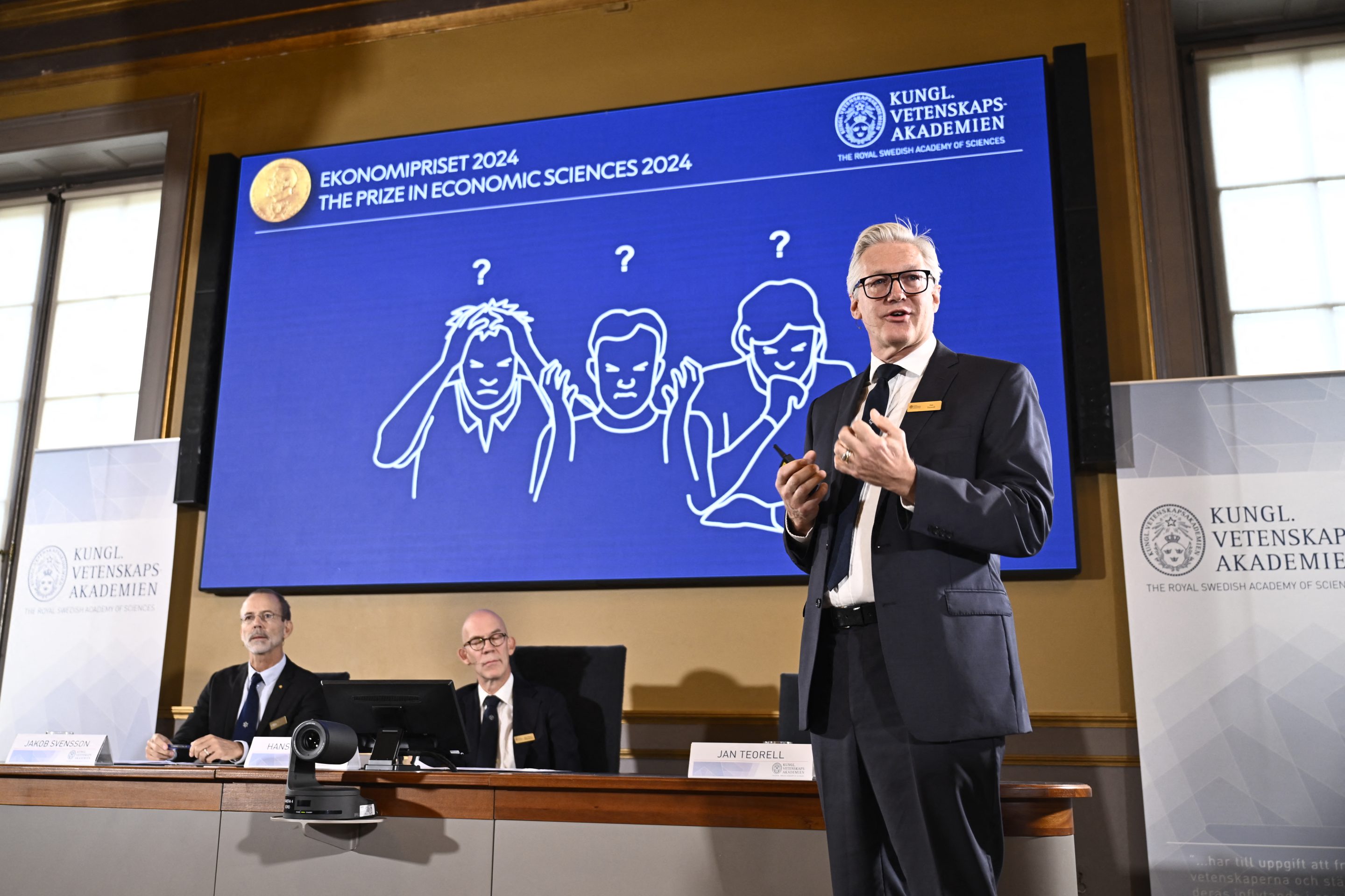 Academy of Sciences permanent secretary Jan Teorel delivers a press conference in front of a screen showing results of the research of laureates of the 2024 Sveriges Riksbank Prize in Economic Sciences in Memory of Alfred Nobel, Daron Acemoglu, Simon Johnson and James A Robinson