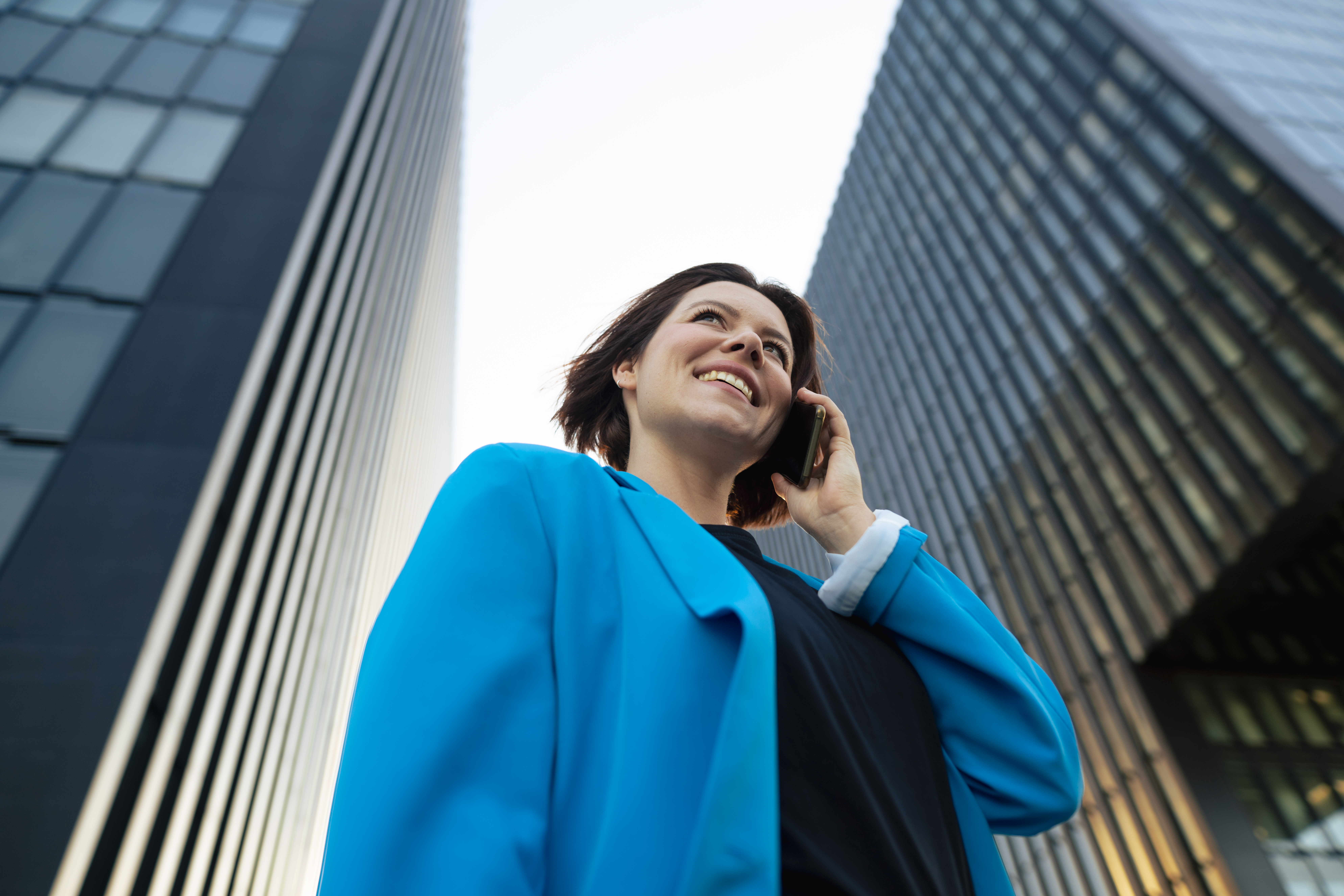 Happy businesswoman talking on mobile phone standing by office building
