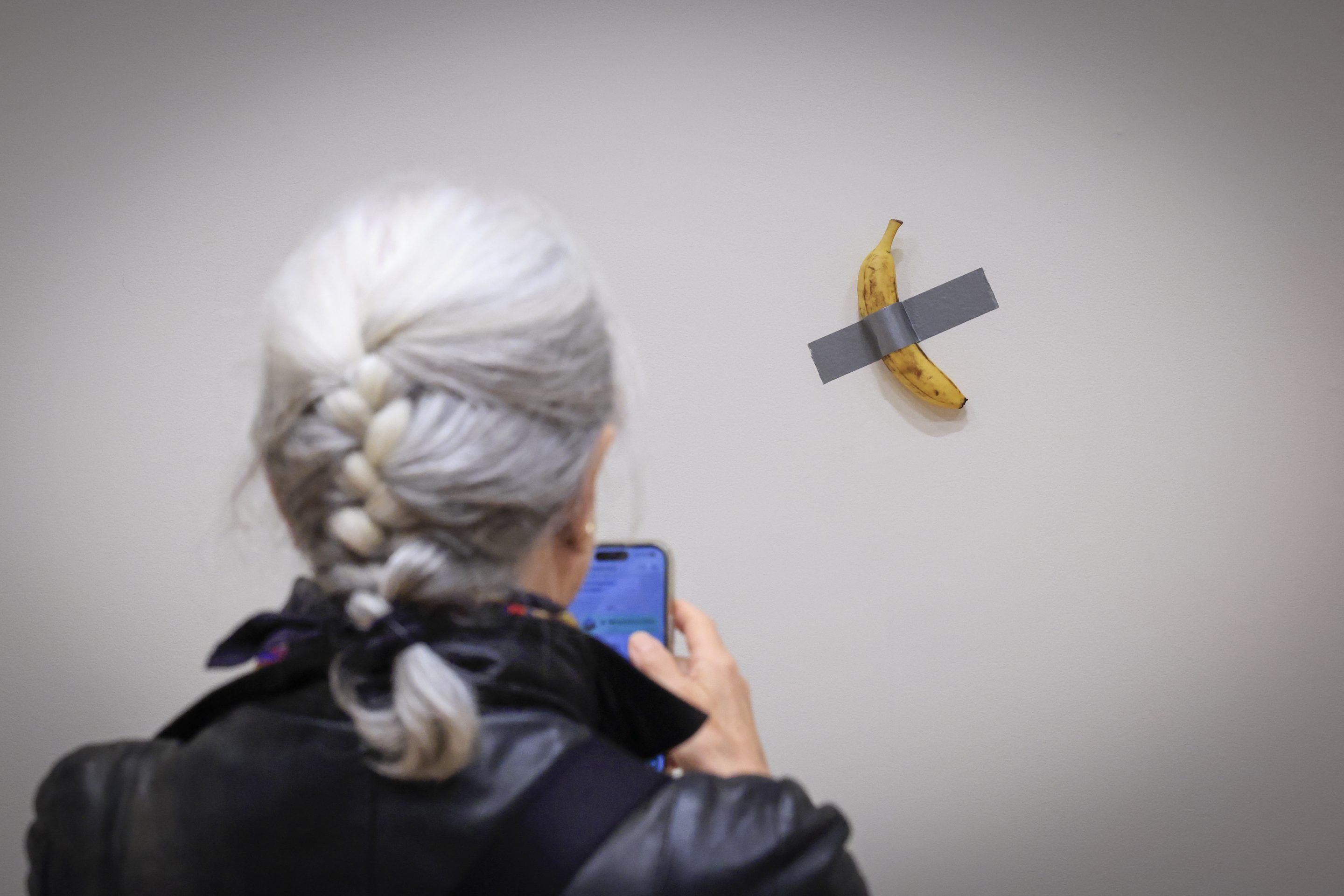 A journalist takes a picture of Italian visual artist Maurizio Cattelan’s duct-taped banana titled “Comedian,” displayed during a media preview at Sotheby’s in New York, on Nov. 8, 2024. 