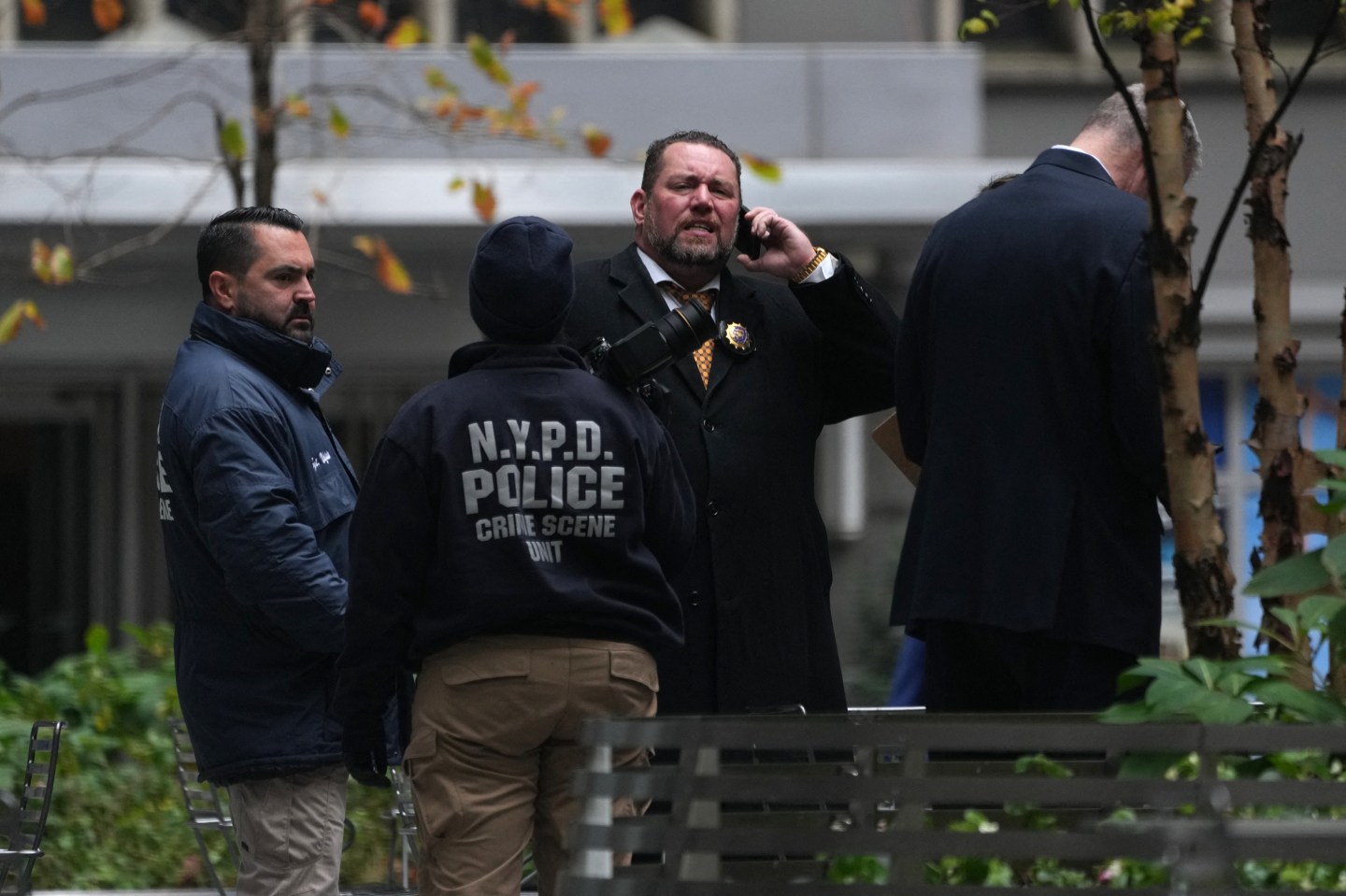 A group of people, including a person in an NYPD jacket, stand outside.