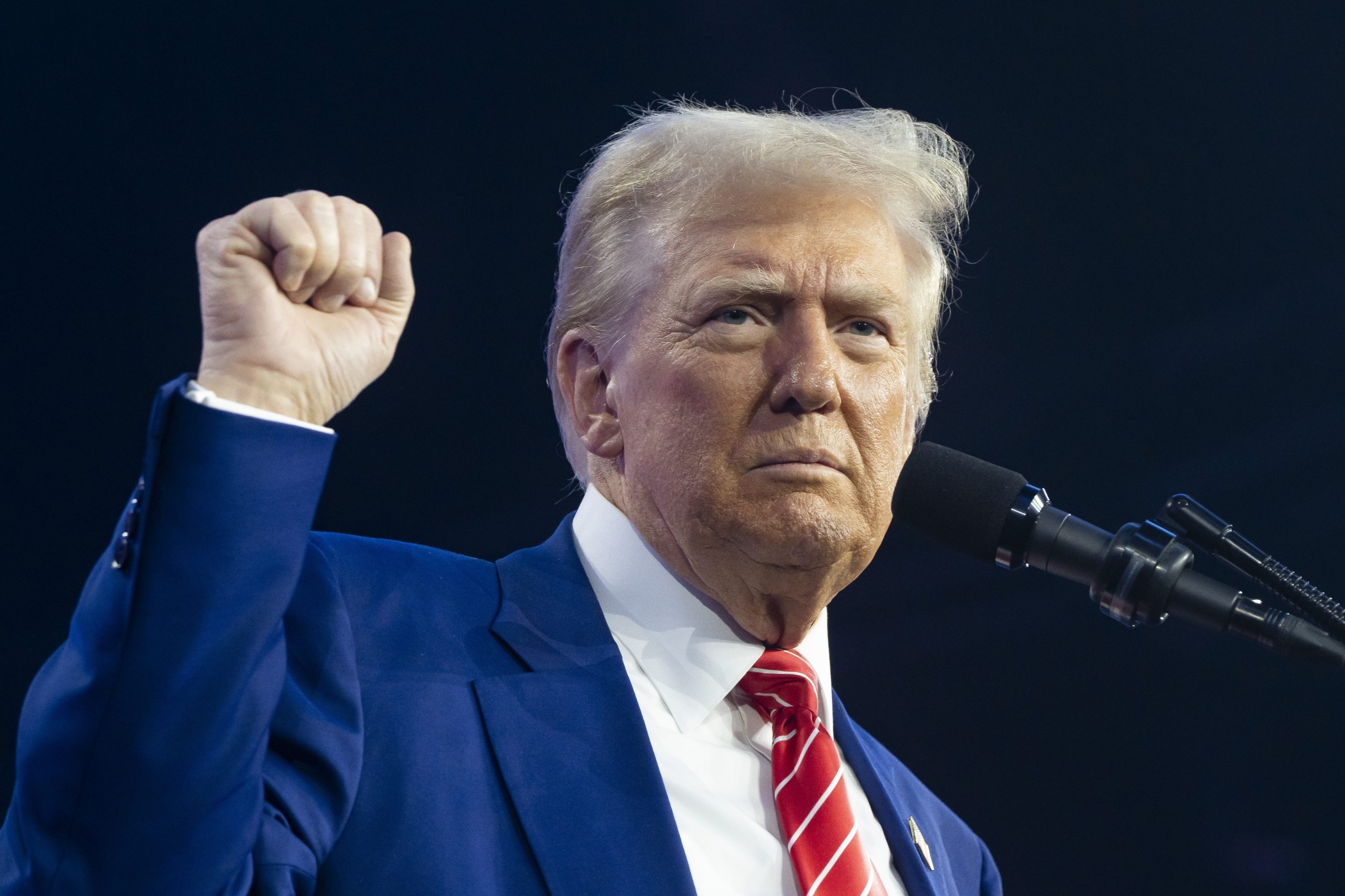 Trump stands in front of a microphone with his fist raised