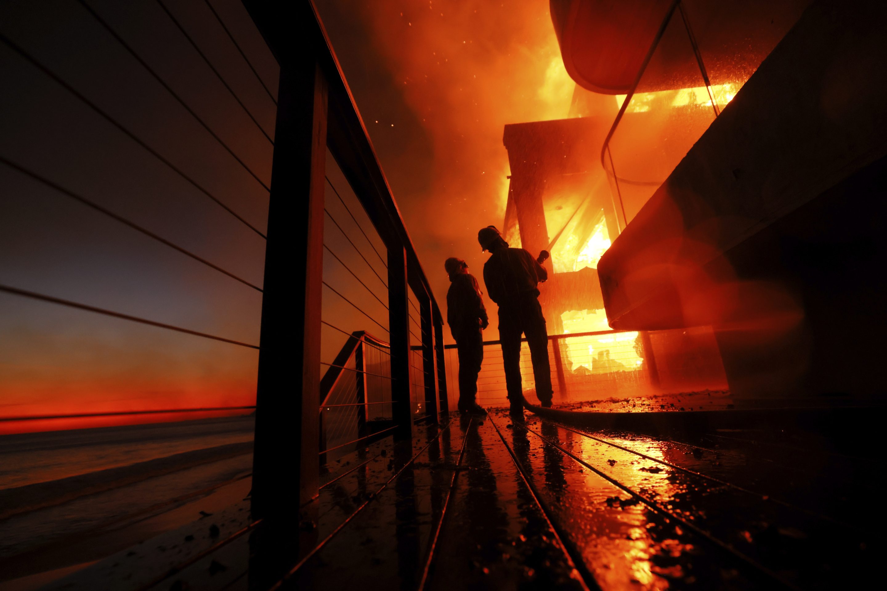 Firefighters work from a deck as the Palisades Fire burns a beach front property on Jan. 8, 2025 in Malibu, Calif.