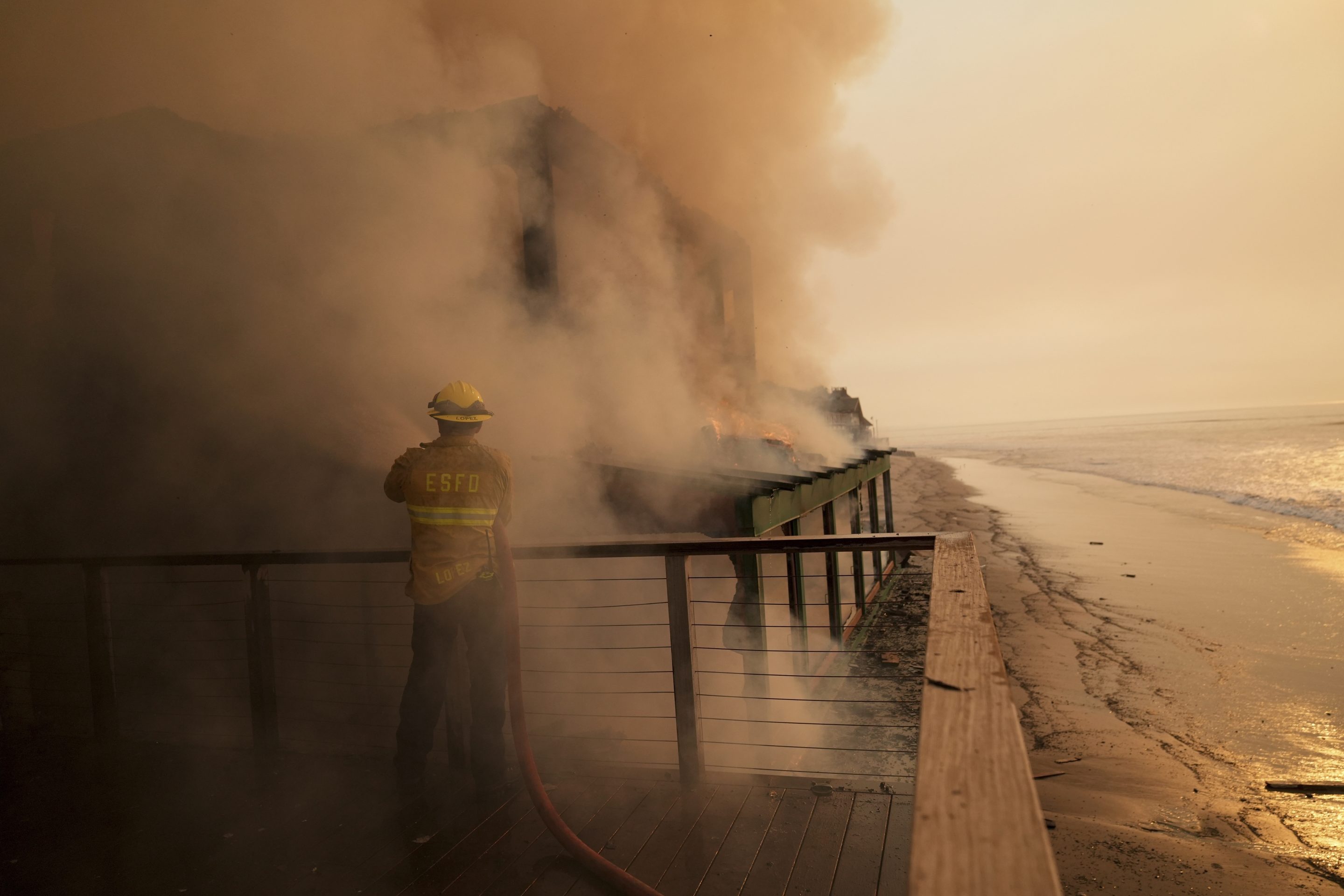 A firefighter protects a beachfront property while fighting the Palisades Fire on Jan. 9, 2025, in Malibu, Calif.