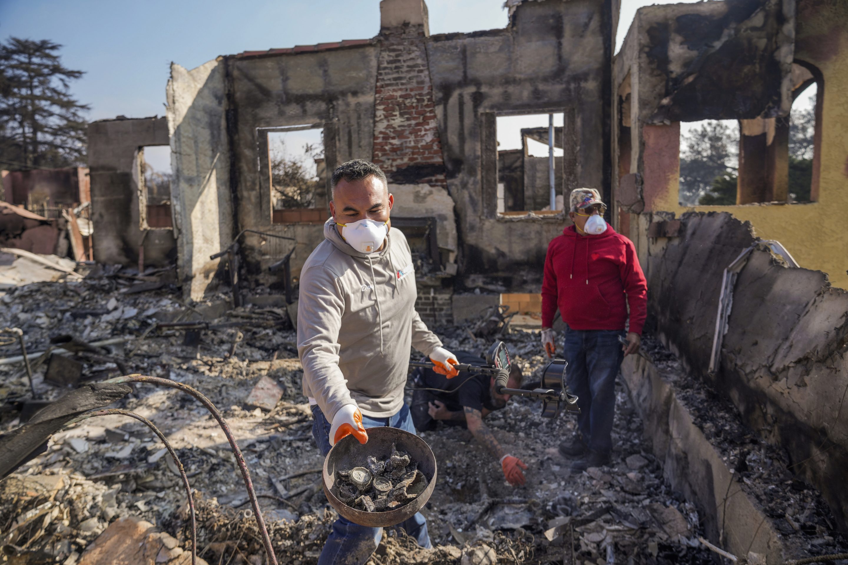 Homeowner David Marquez, left, holds a metal detector as he shows recovered metal items found with his father, Juan Pablo Alvarado, right, inside the walls of their multi-generational home in the aftermath of the Eaton Fire, on Jan. 19, 2025, in Altadena, Calif.