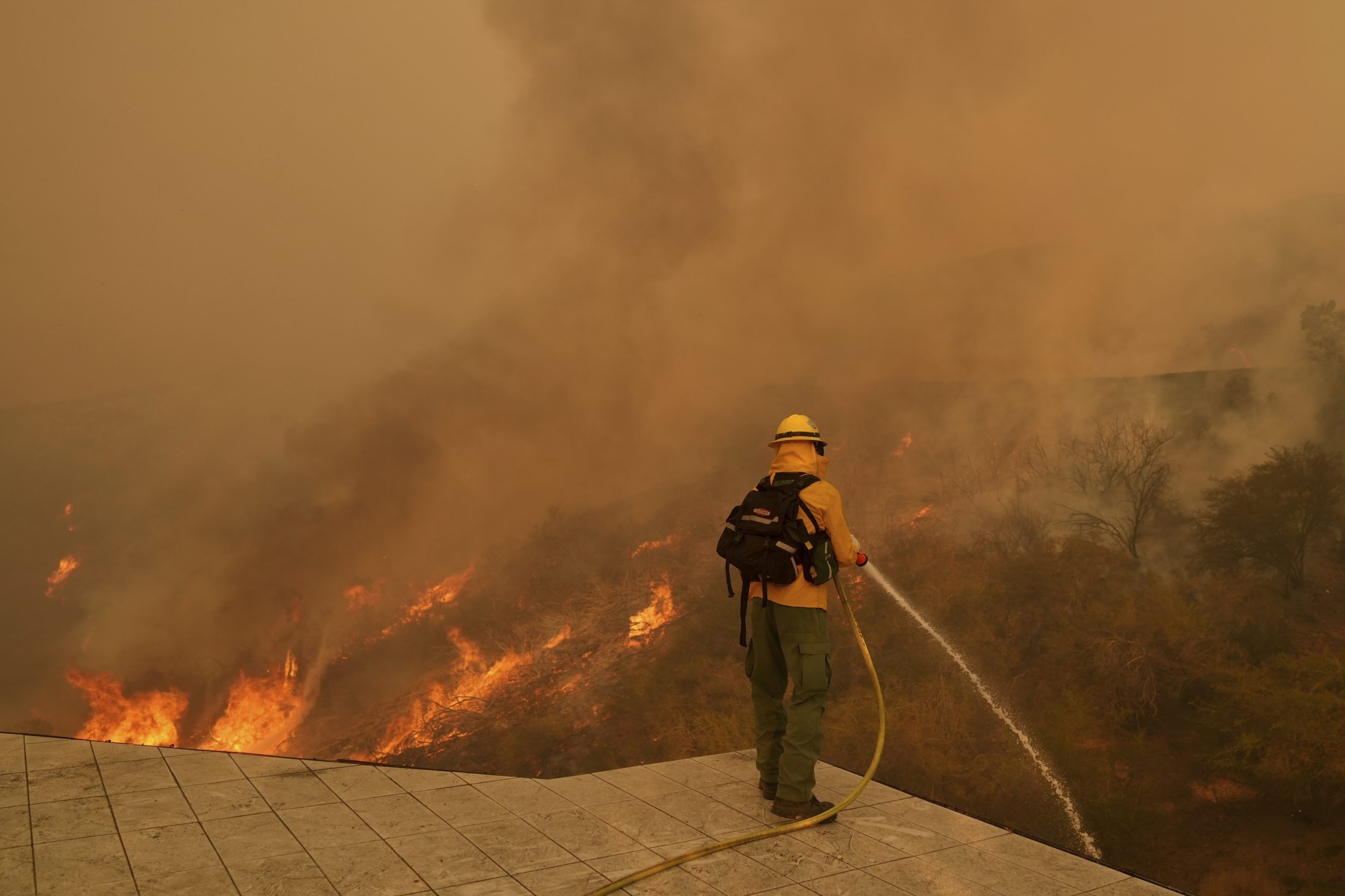 A firefighter hoses down flames as the Palisades Fire approaches in Mandeville Canyon, Jan. 11, 2025, in Los Angeles. 