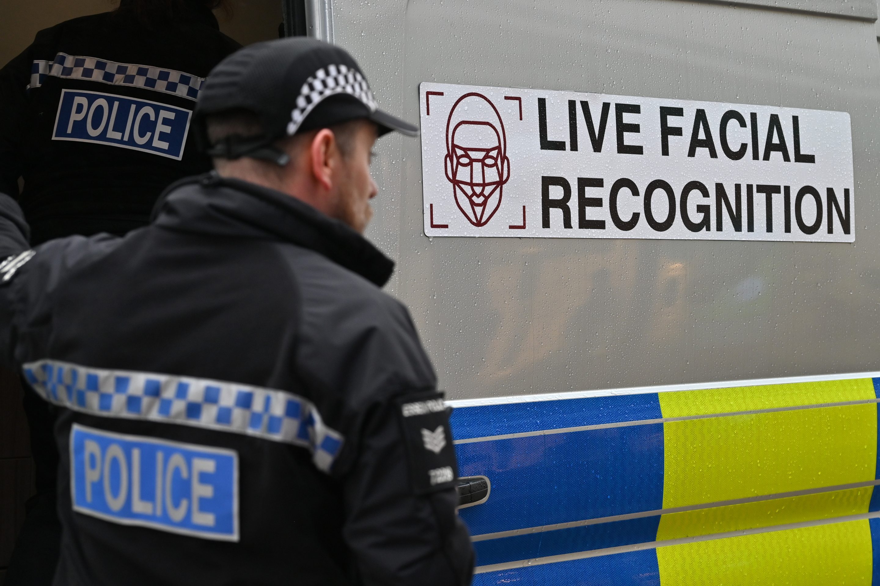A British police officer stands in front of a police van with a sign warning the public that the police are using live facial recognition technology.
