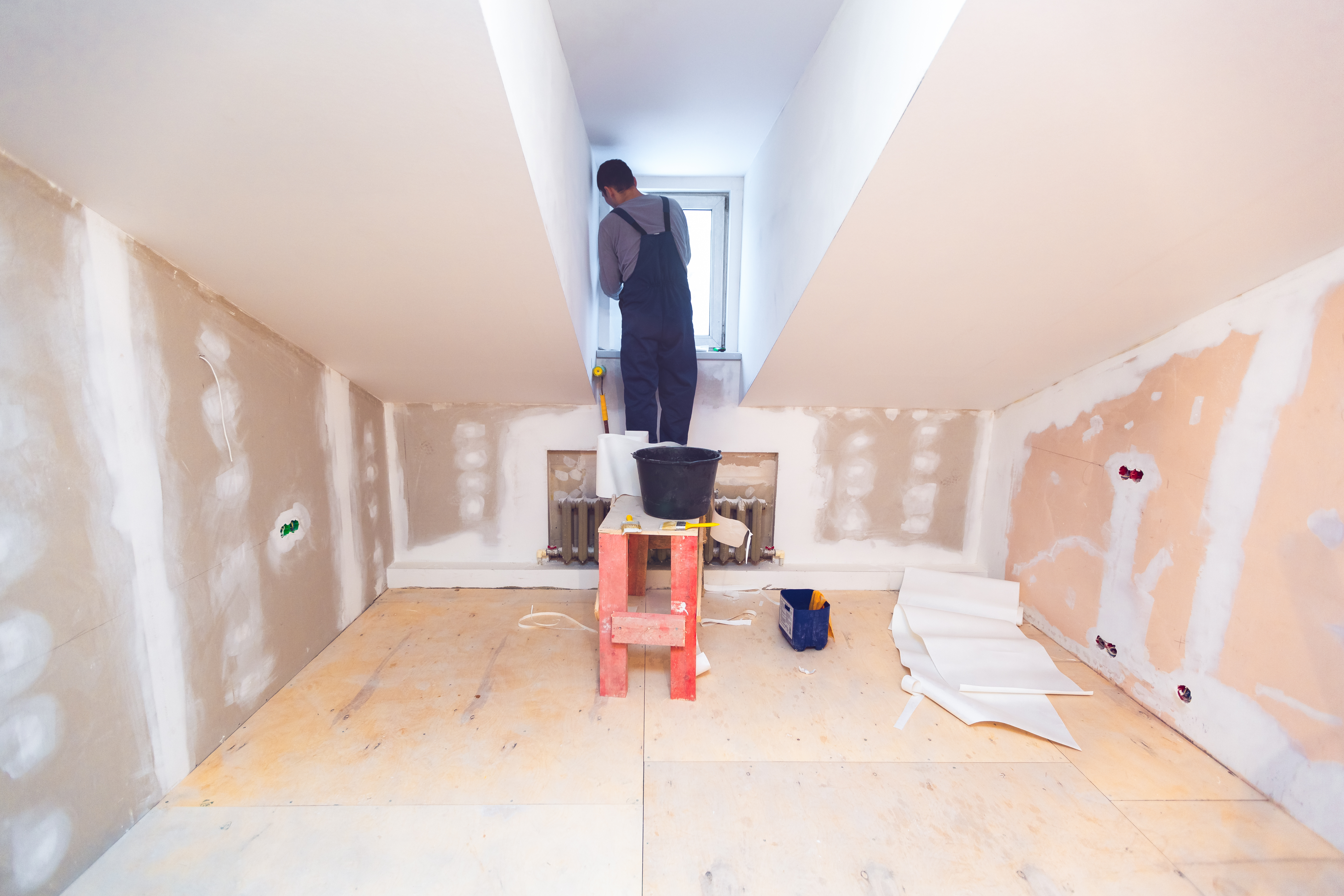 Worker is installing pvc window from wooden platform in small room of apartment that is under construction