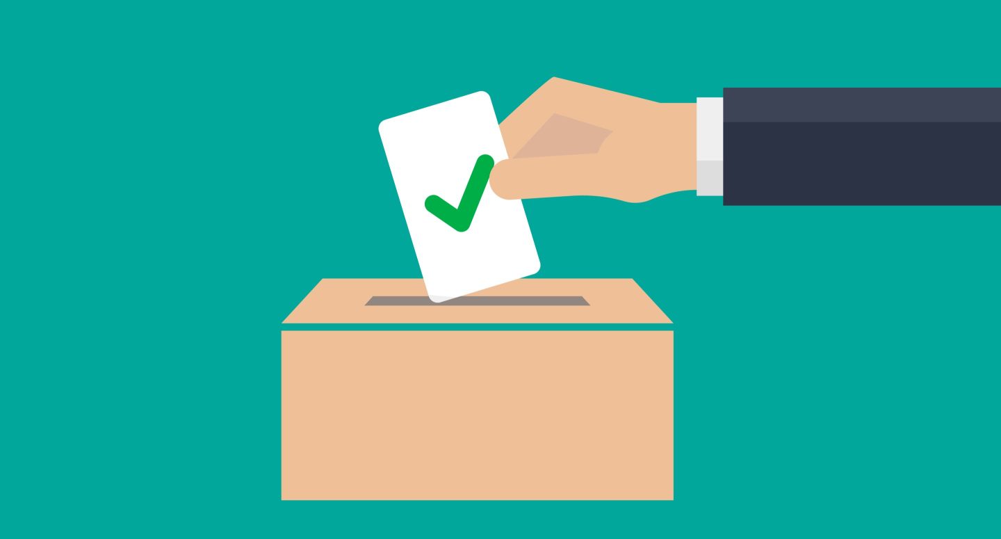 A man's hand placing a ballot with a check mark in the ballot box.