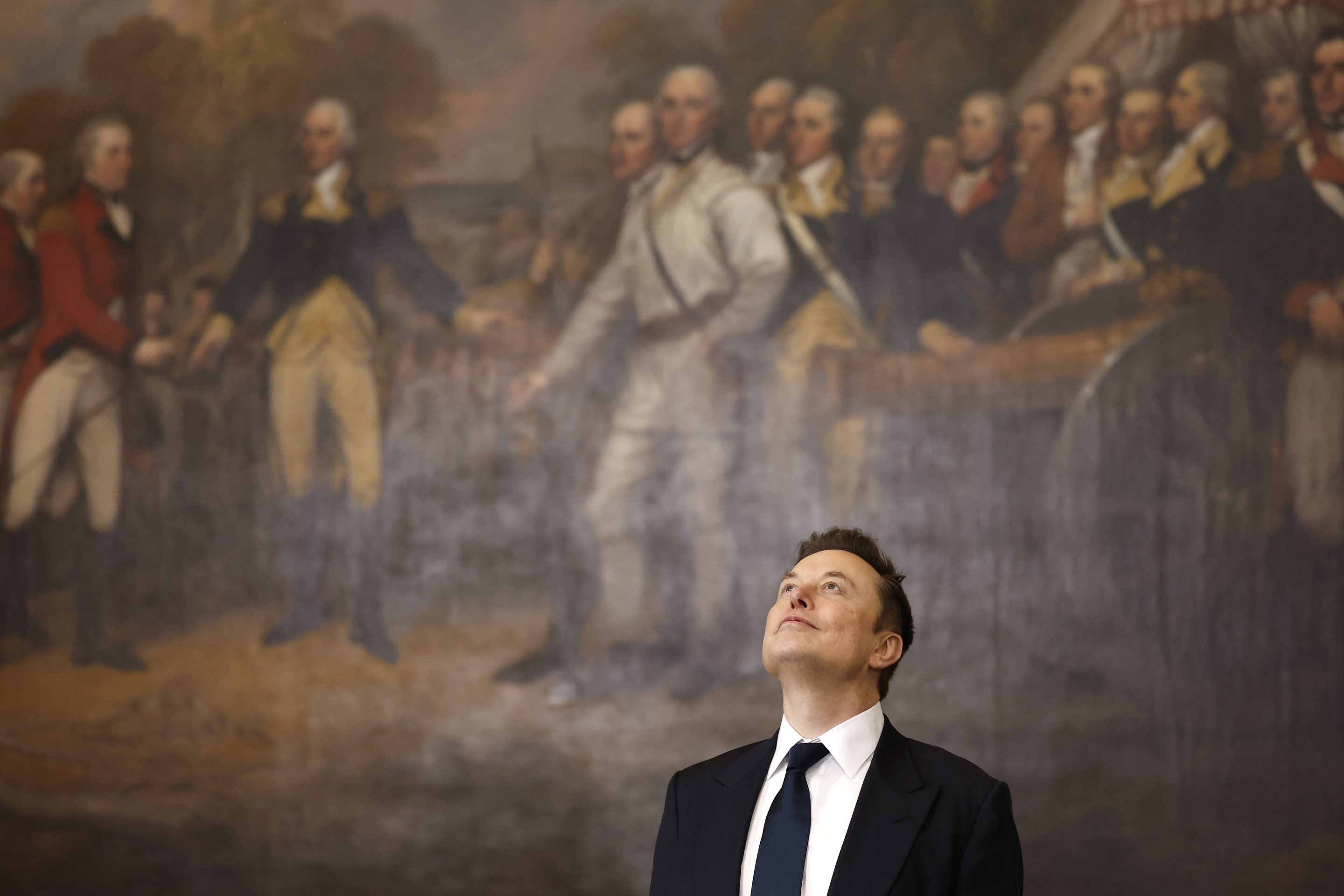 Elon Musk in front of a large mural of the U.S. founding members.