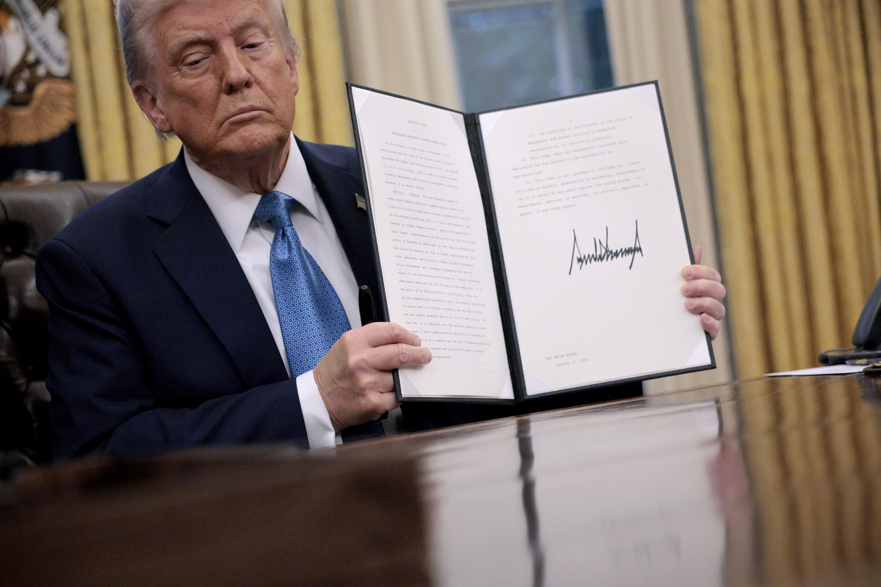 President Donald Trump hold up an executive order, "Unleashing prosperity through deregulation," that he signed in the Oval Office on January 31, 2025 in Washington, DC. Trump spoke to reporters about tariffs against China, Canada and Mexico and how the newly confirmed Interior Secretary Doug Burghum will coordinate with the Energy Department and the Environmental Protection Agency.