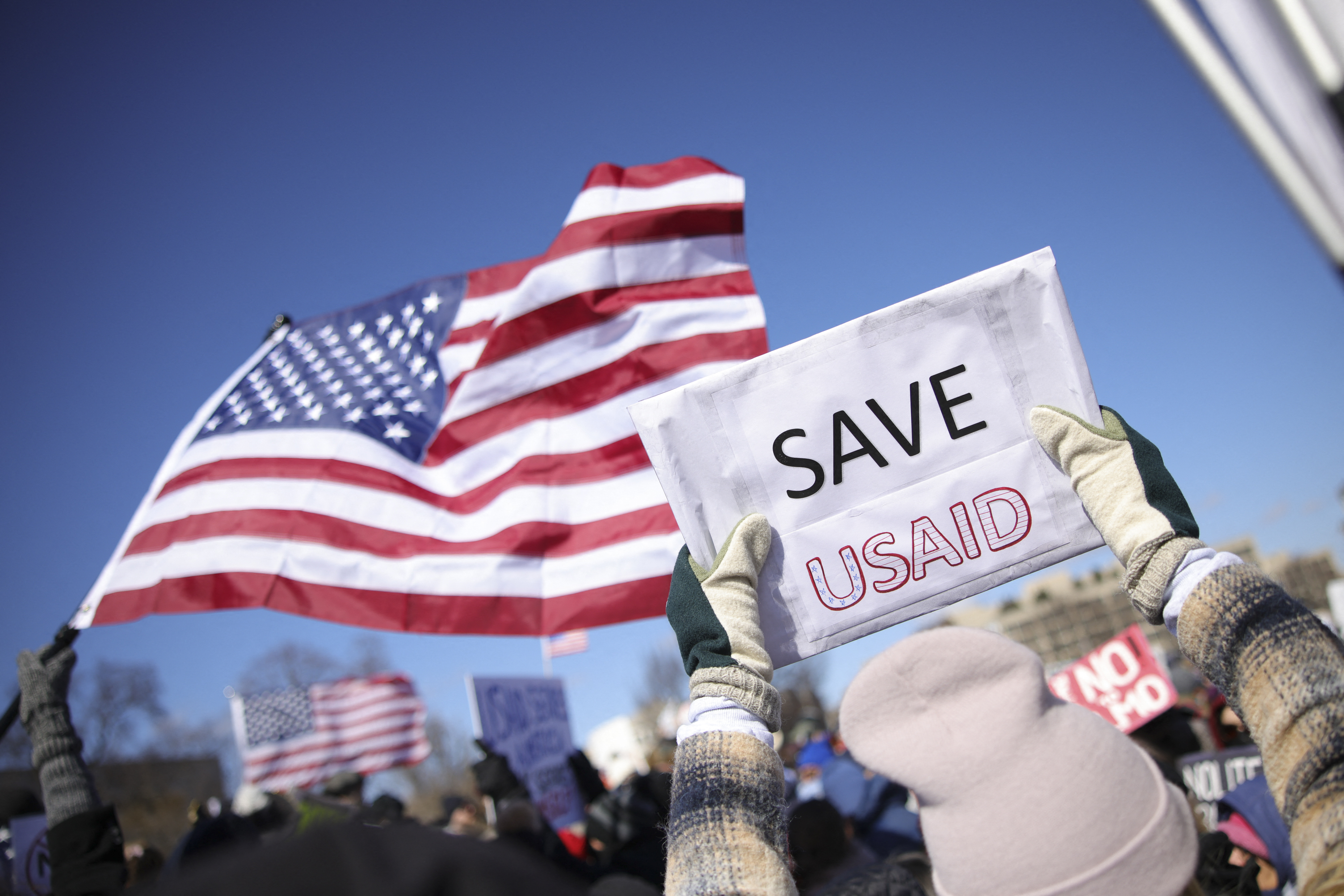 Picture of the US flag behind a sign saying "Save USAID."