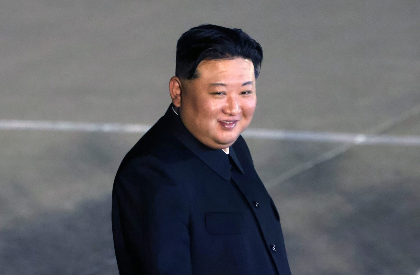 Kim Jong Un smiles at the camera as he walks outside.