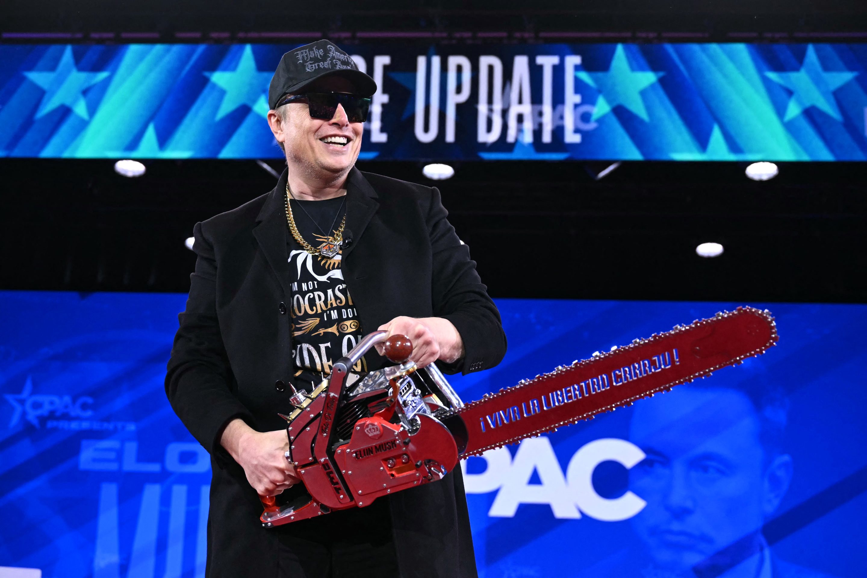 Elon Musk smiles while wielding a chainsaw
