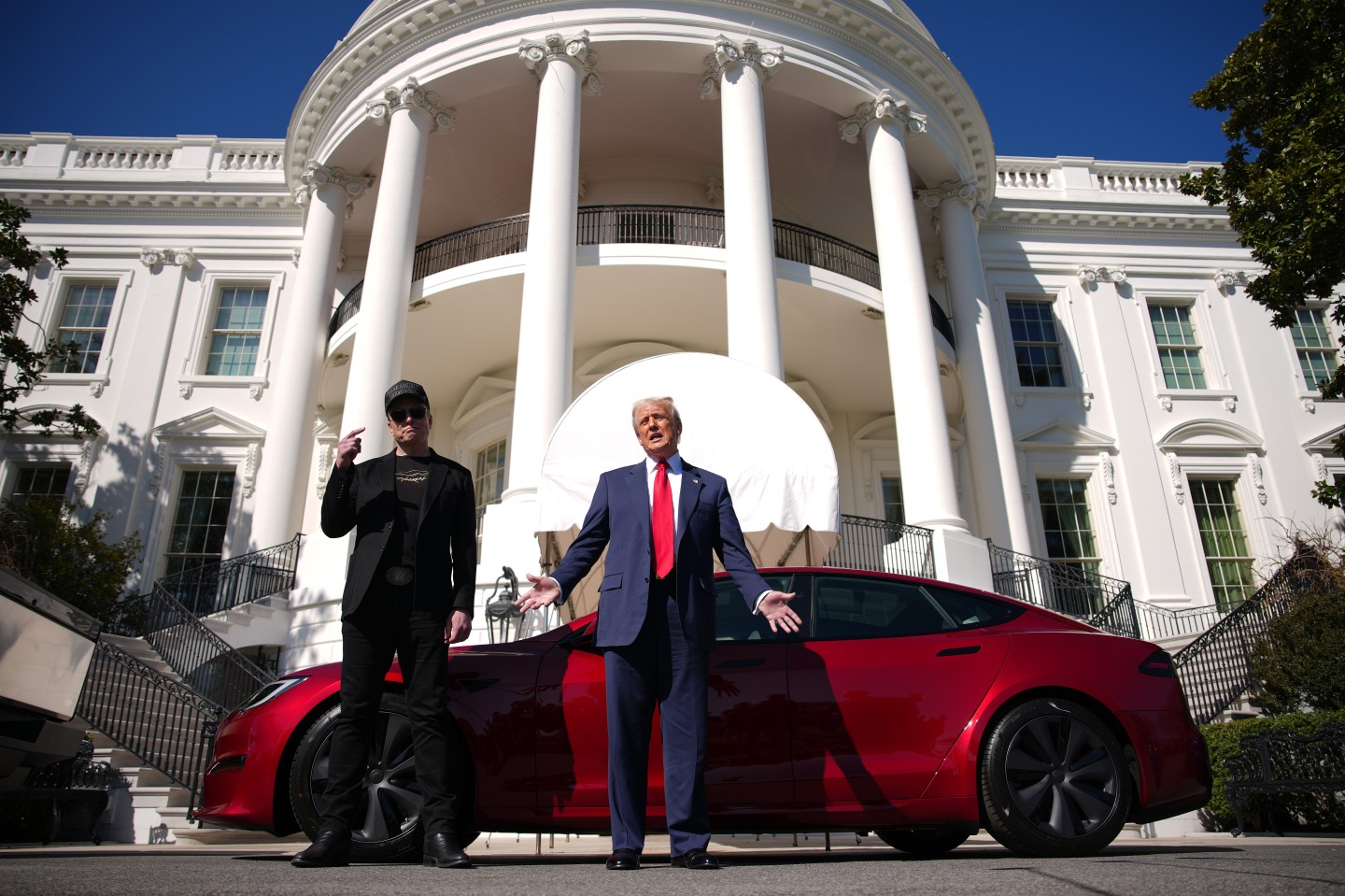 Elon Musk and Donald Trump stand in front of a red Tesla outside the White House